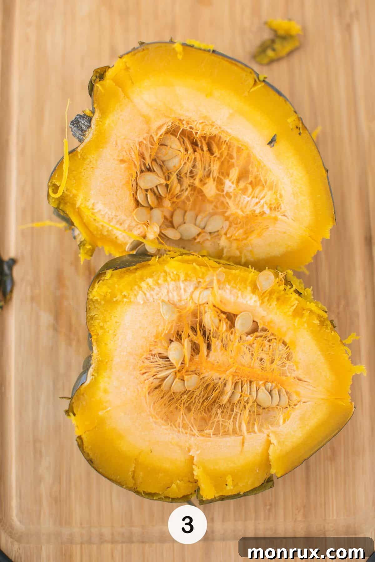 A cooked acorn squash, now easily cut in half on a cutting board, with seeds being scooped out.