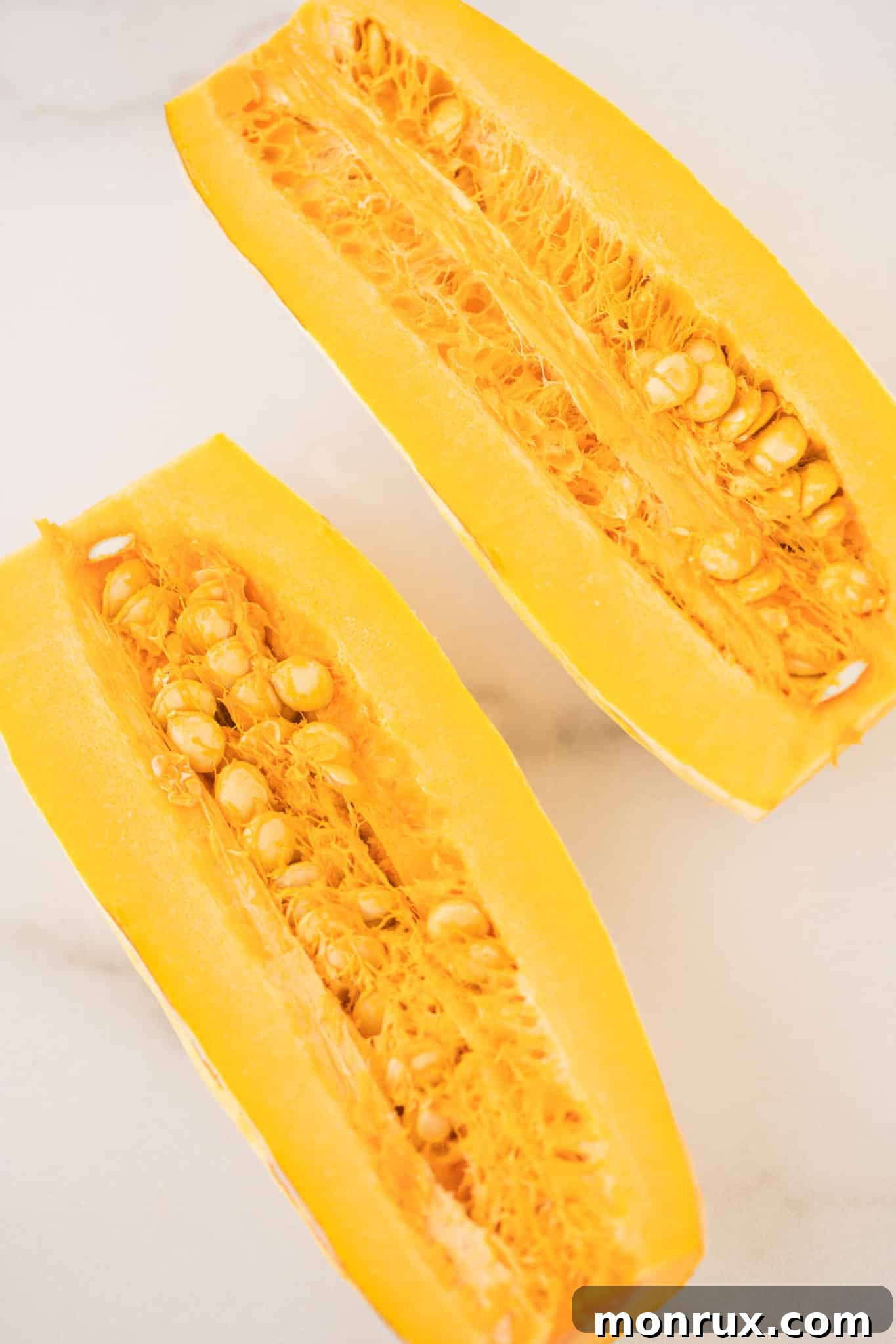 A fresh delicata squash meticulously cut in half lengthwise on a cutting board, revealing its interior.