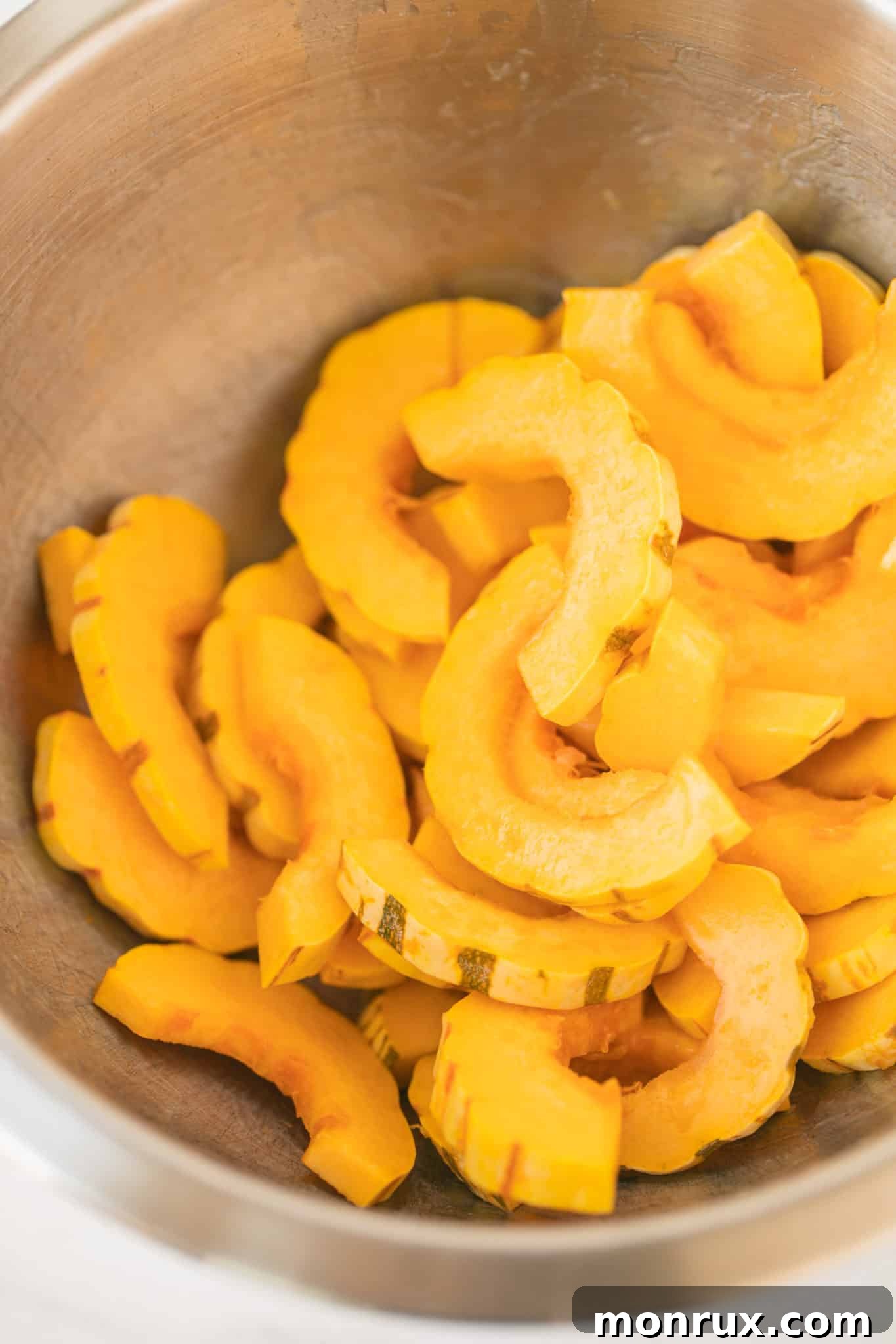 Neatly sliced delicata squash half-moons in a mixing bowl, prepared for seasoning.