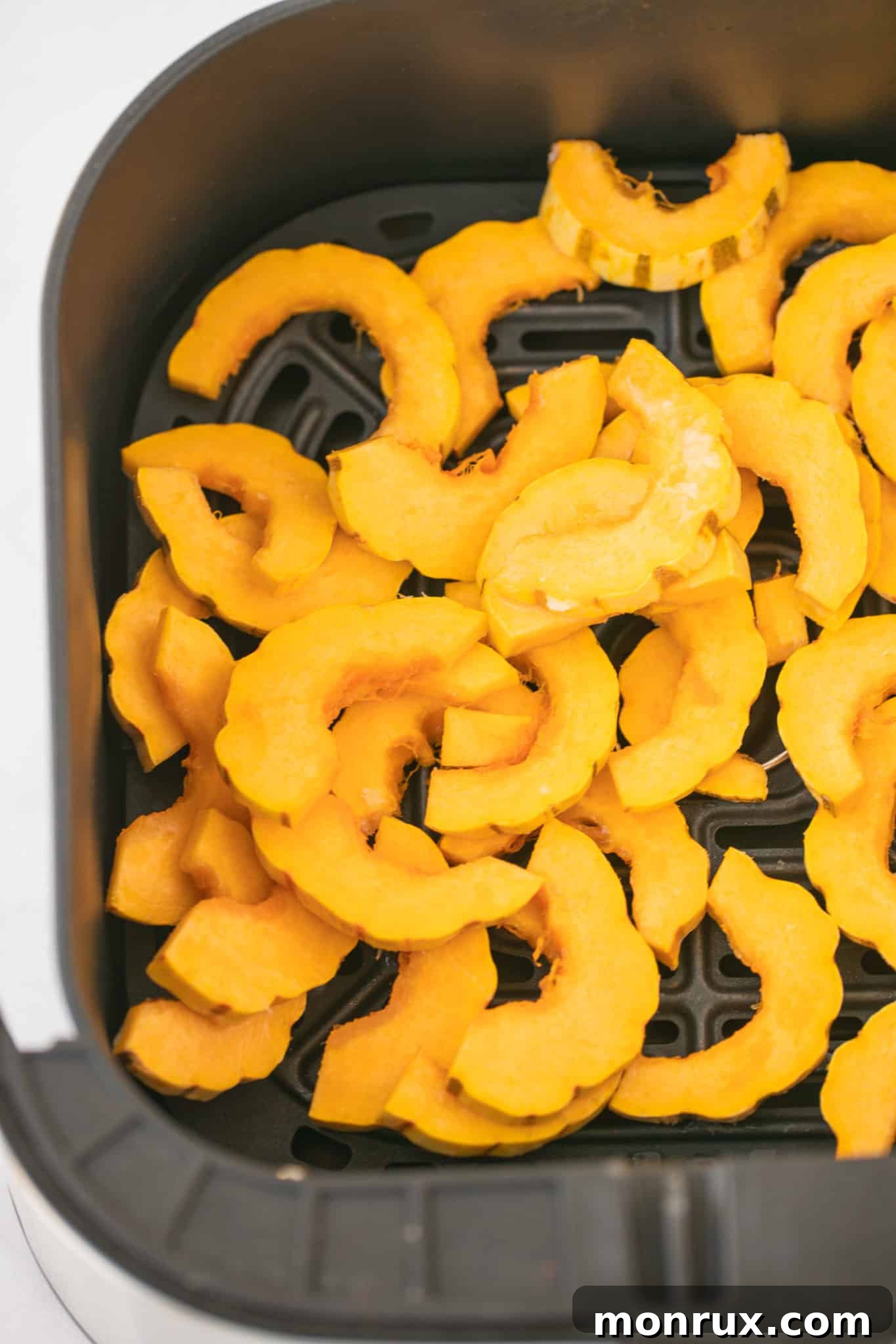 Seasoned delicata squash slices arranged in the basket of an air fryer, ready for cooking.