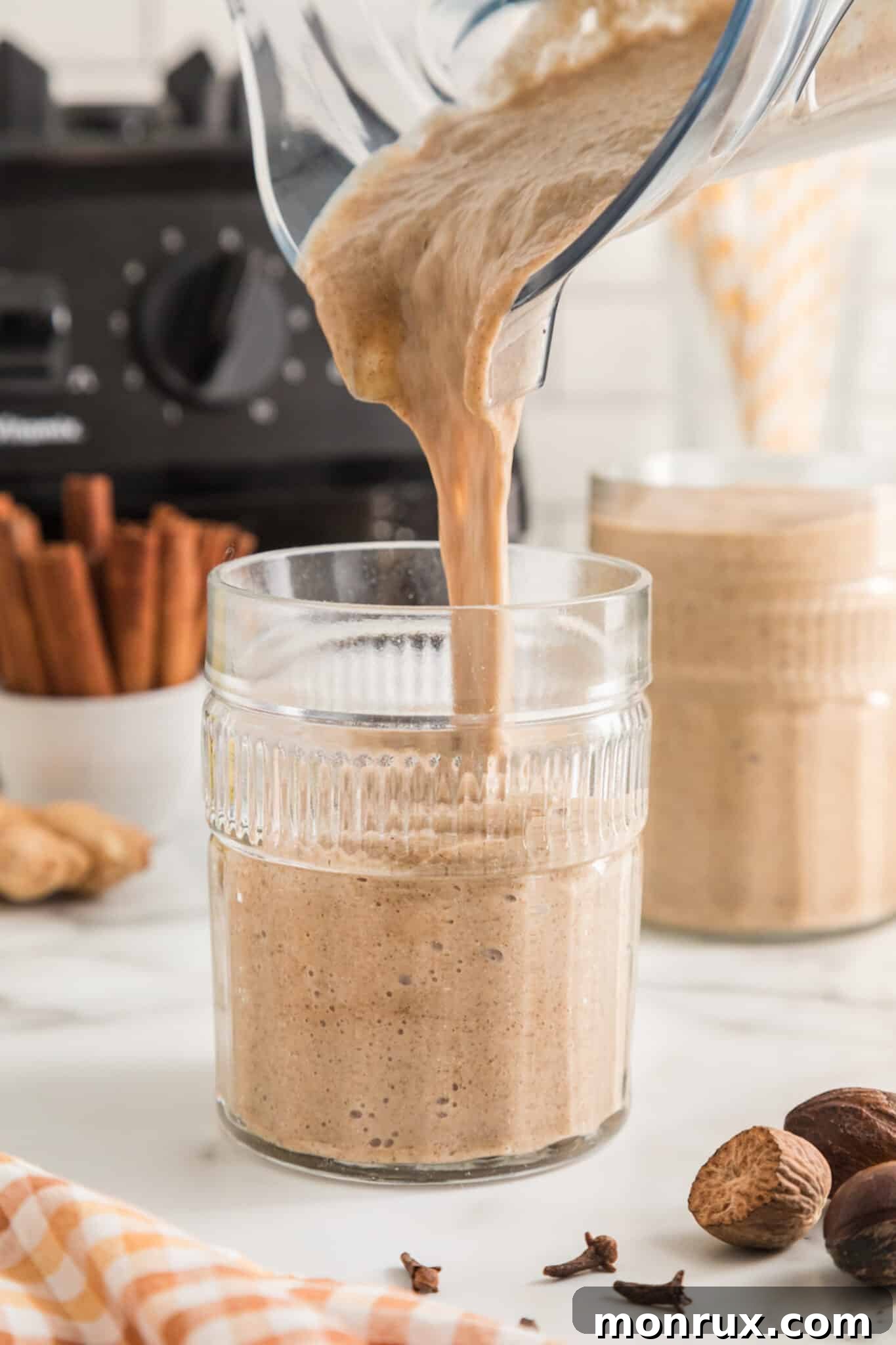A blender jar elegantly pouring the perfectly smooth gingerbread smoothie into a waiting glass.