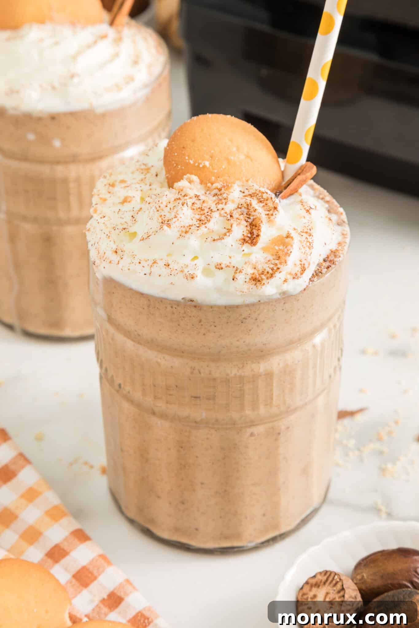 Two glasses of gingerbread smoothie topped with whipped cream and cookies, presented beautifully.
