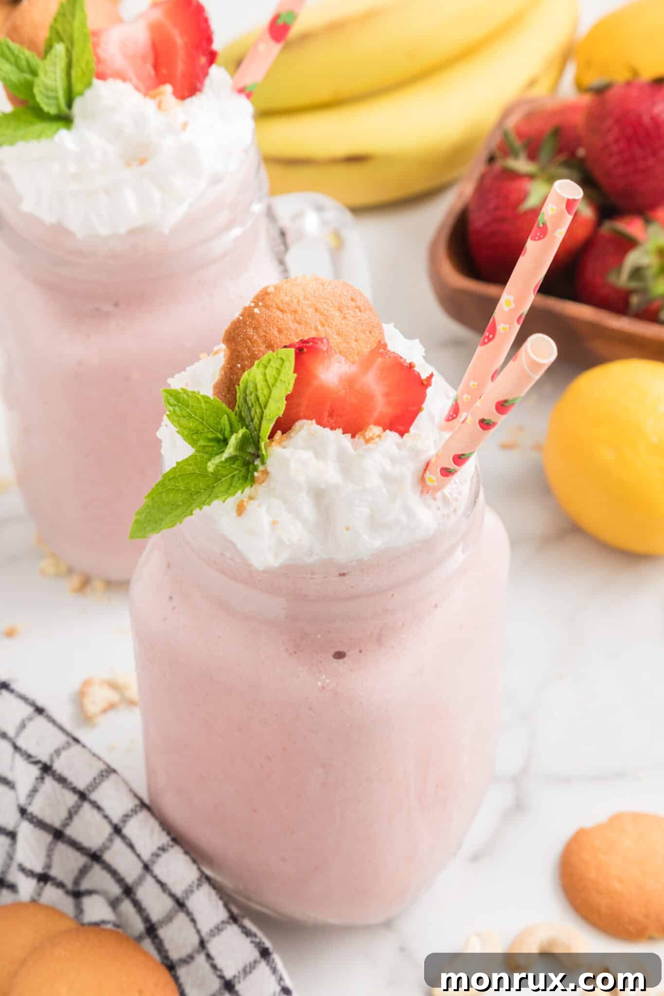Vegan Strawberry Cheesecake Smoothie elegantly served in a handled mason jar with two straws, garnished with whipped cream and crushed cookies.