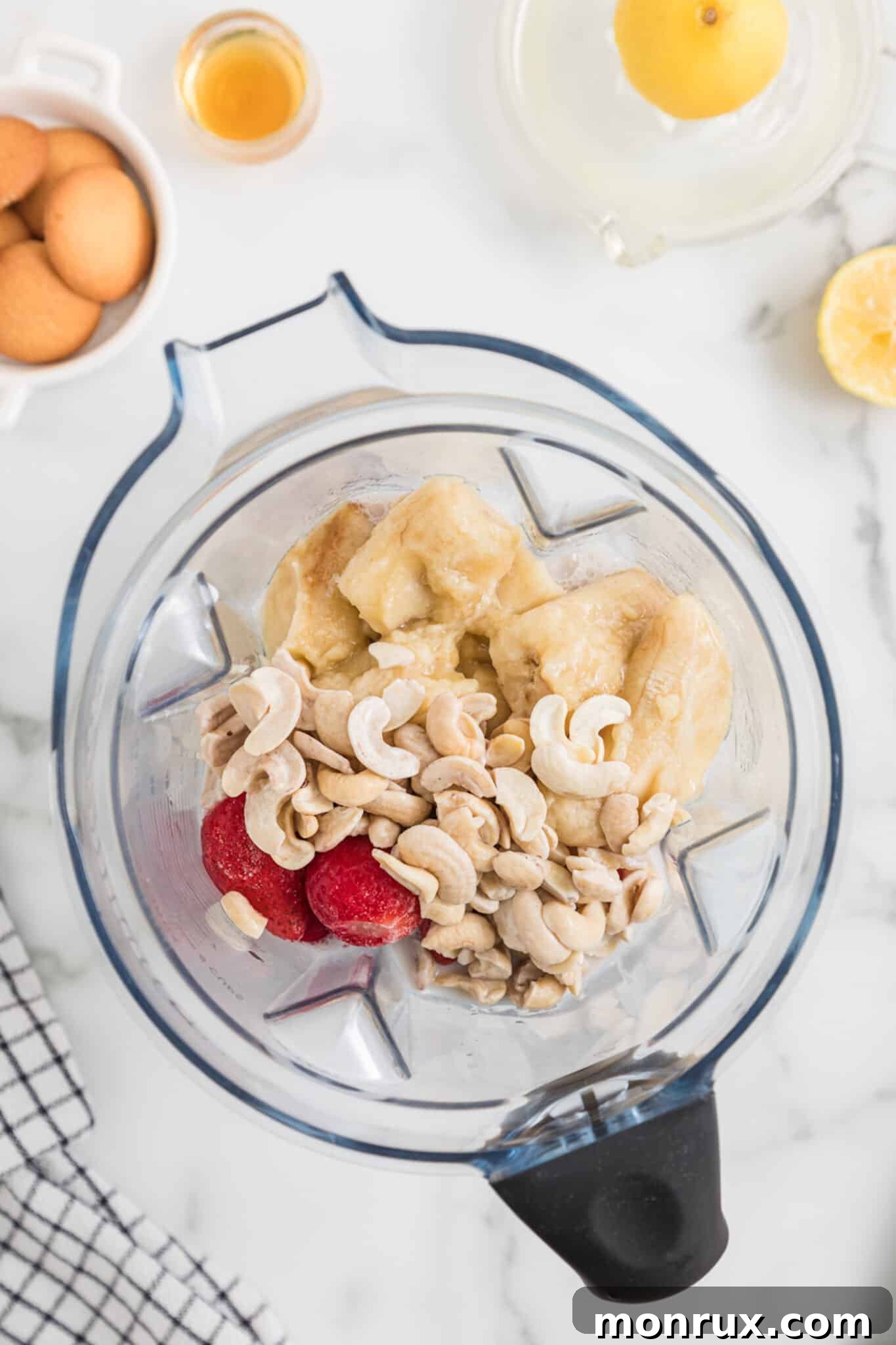 A high-speed blender jar, meticulously filled with a colorful array of ingredients, poised to create a Strawberry Cheesecake Smoothie.