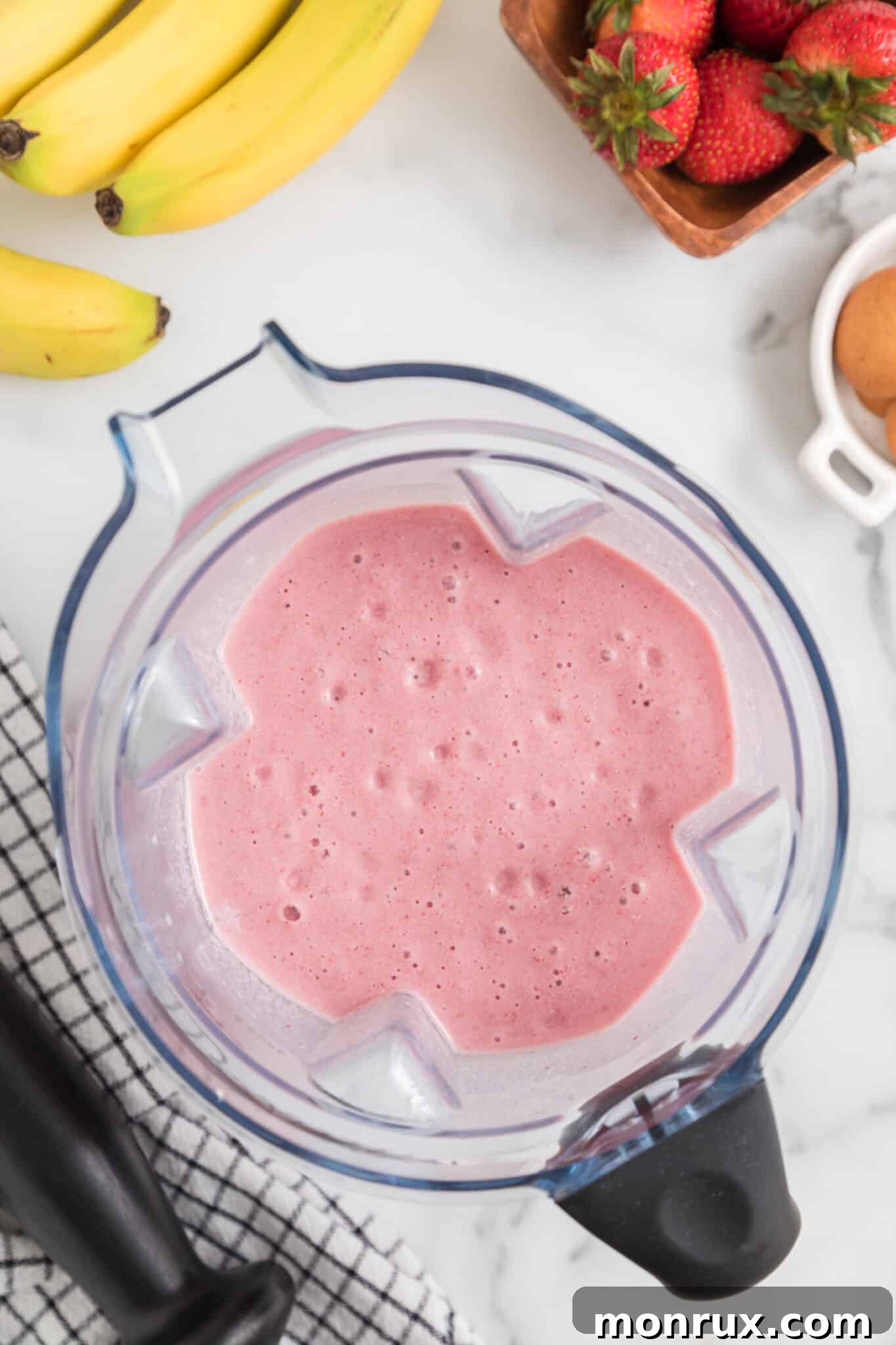 A top-down view of a blender jar, brimming with a perfectly smooth, vibrant pink blended strawberry cheesecake smoothie.