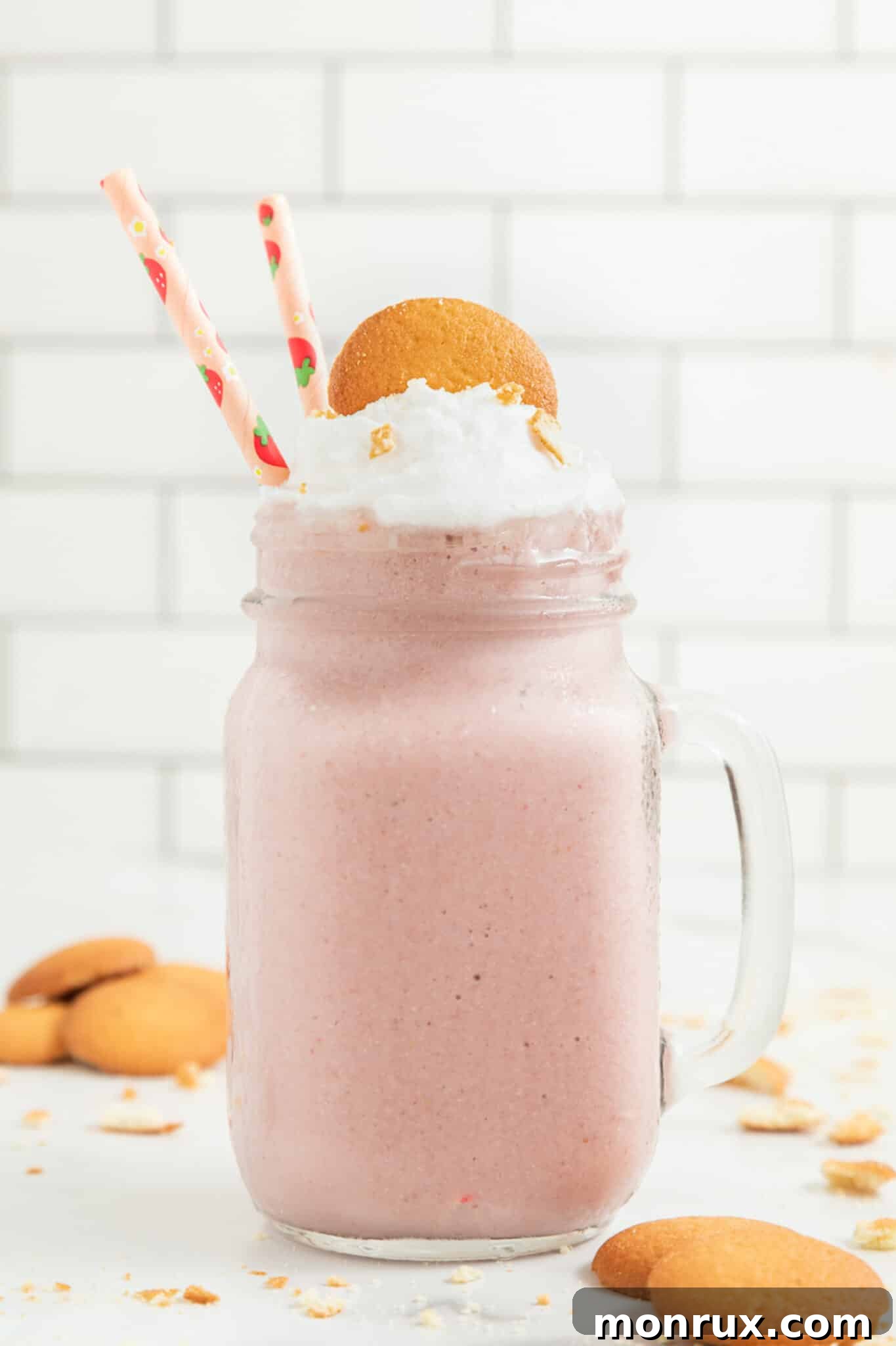 A refreshing Vegan Strawberry Cheesecake Smoothie, perfectly presented in a handled mason jar with two striped straws, ready to be enjoyed.
