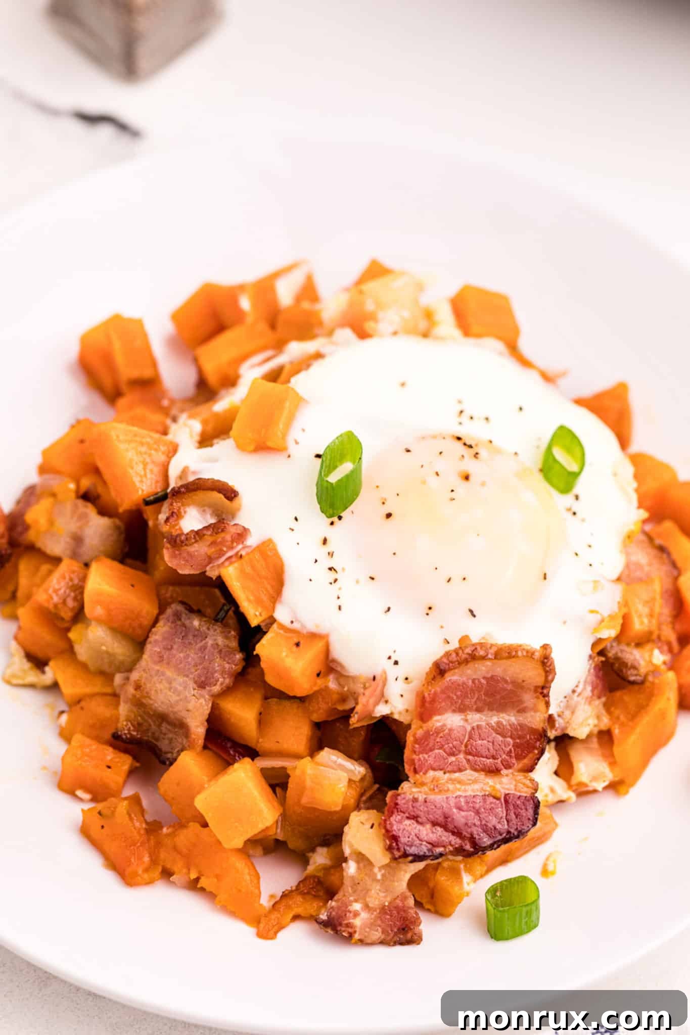 A vibrant bowl of Sweet Potato Apple Hash, topped with a perfectly cooked egg, ready to be enjoyed on a rustic table.