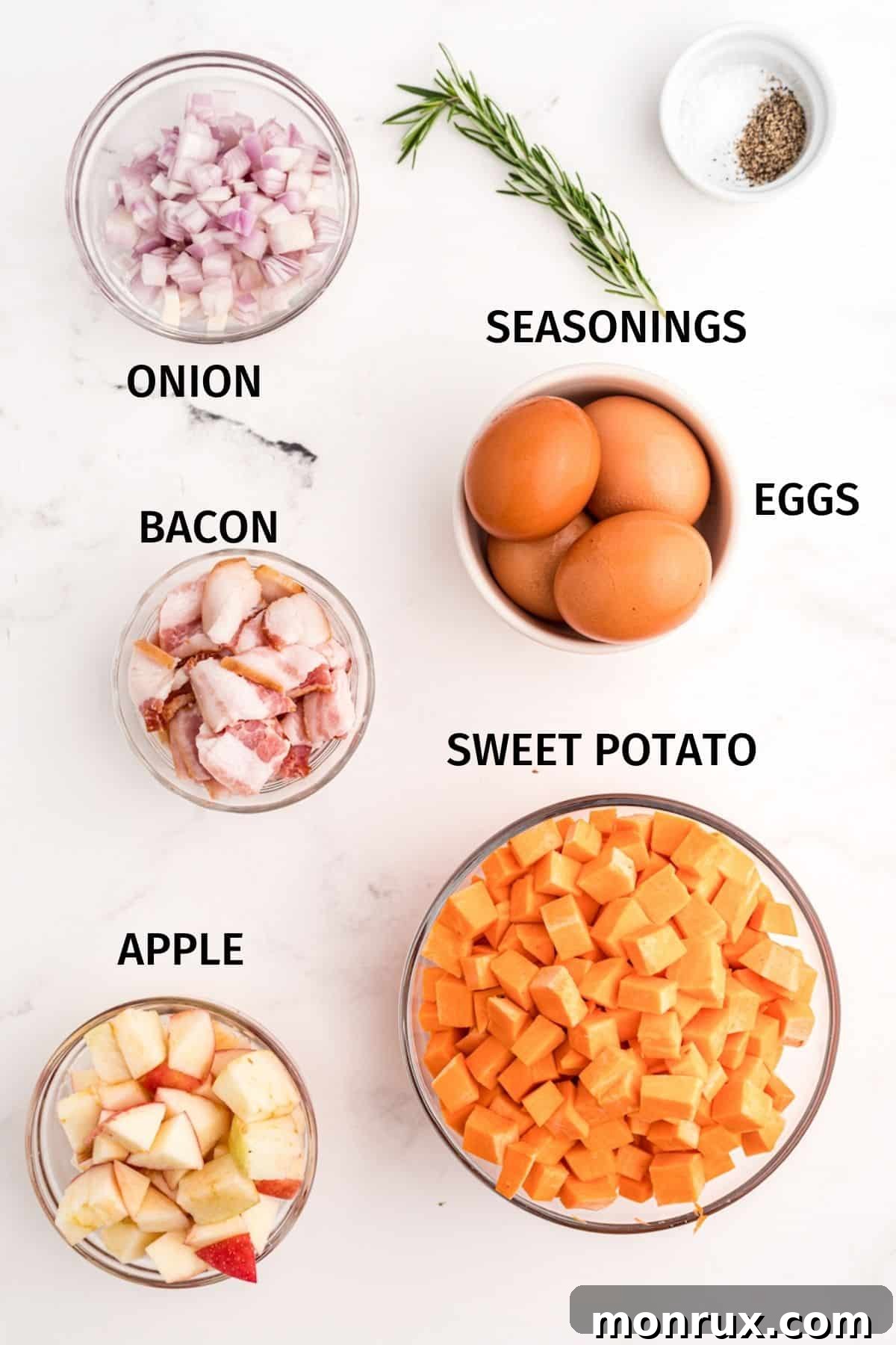 A curated selection of fresh, raw ingredients laid out for making Sweet Potato Apple Hash, featuring vibrant sweet potatoes, crisp apples, strips of bacon, an onion, fresh rosemary sprigs, and seasoning essentials.