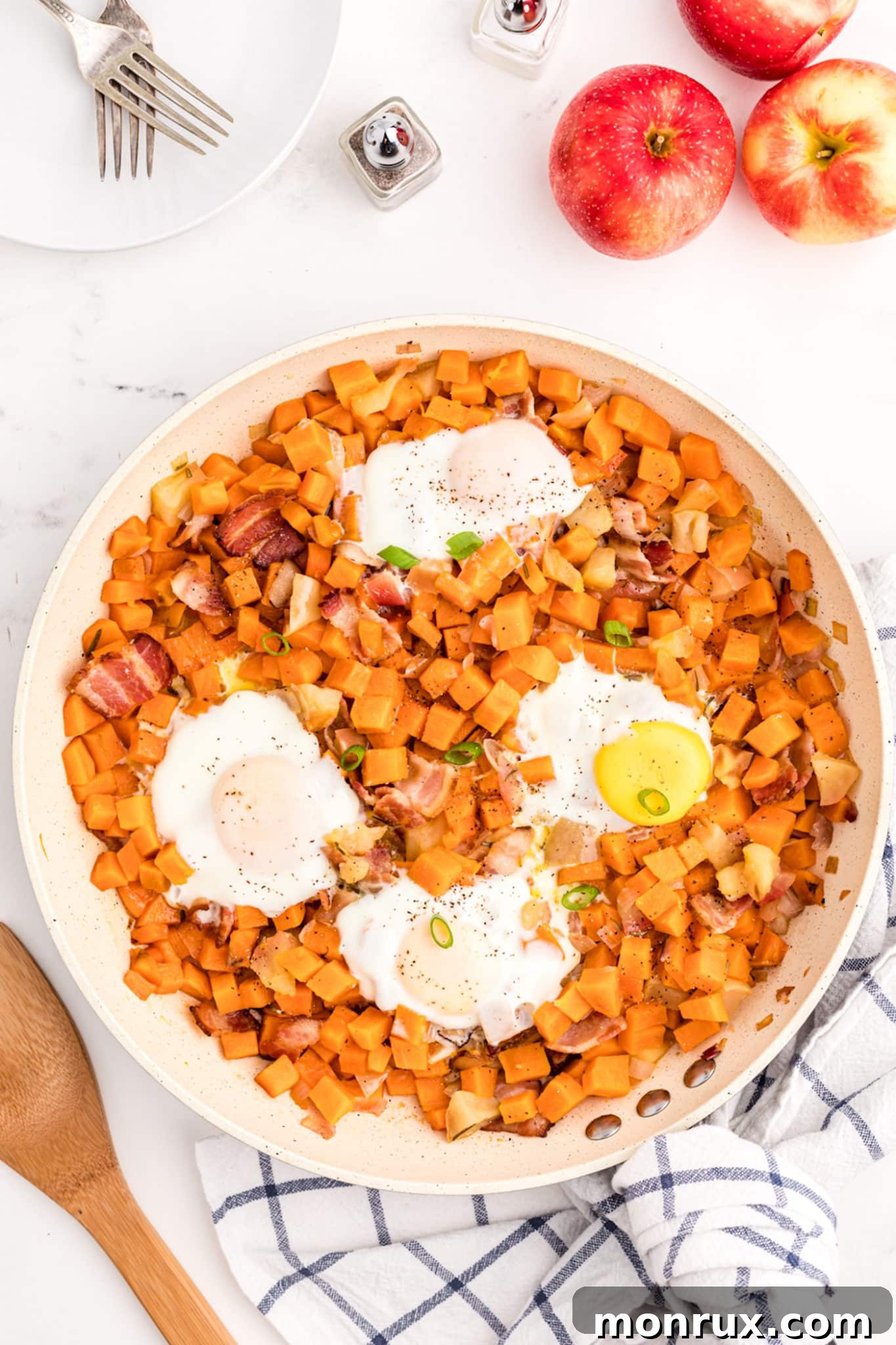 A close-up shot of perfectly cooked fried eggs nestled on top of the Sweet Potato Apple Hash in a skillet, garnished with fresh herbs, ready to be enjoyed.