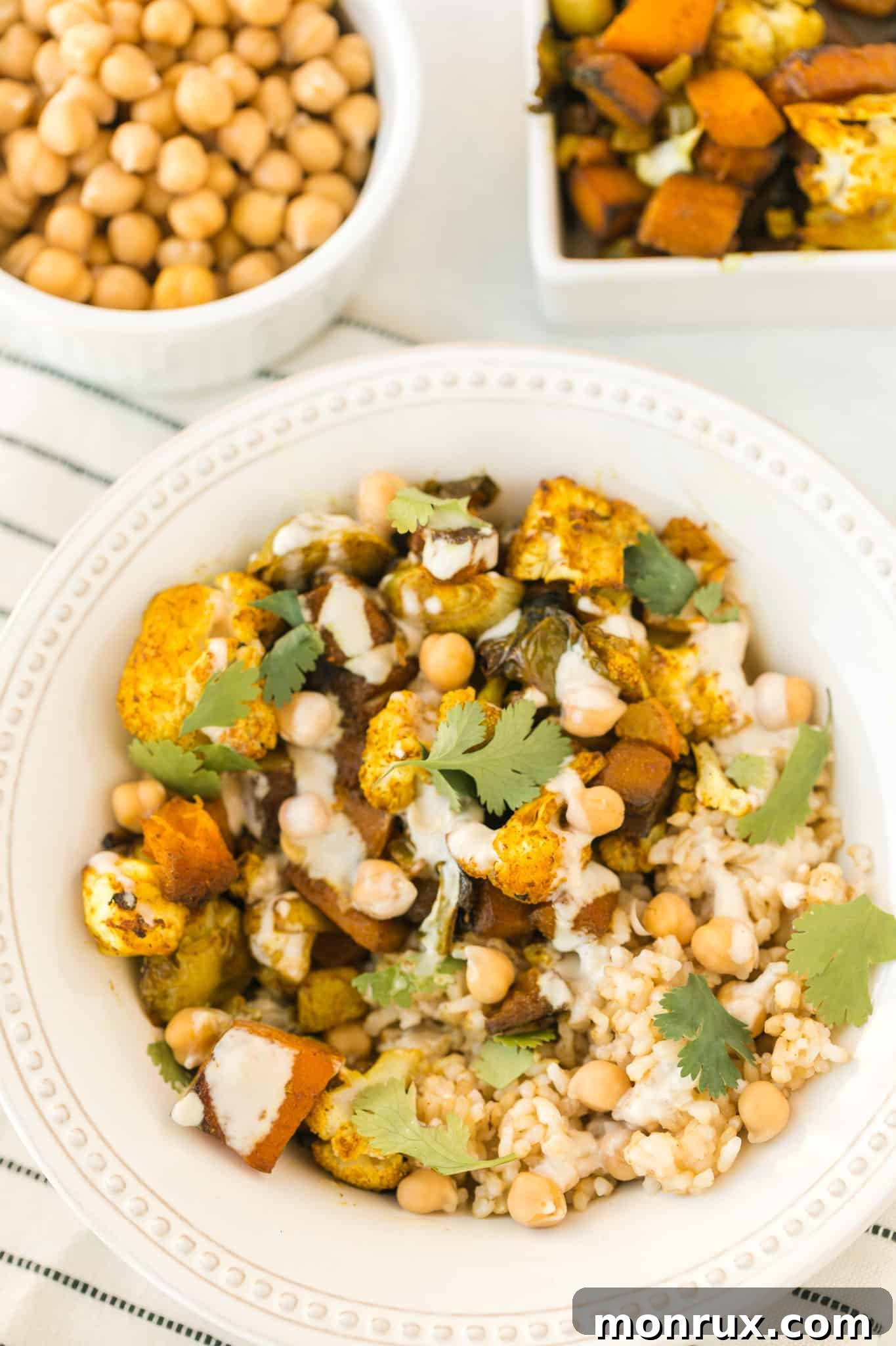A vibrant anti-inflammatory veggie bowl generously served with fluffy brown rice, seasoned chickpeas, and a creamy lemon tahini sauce drizzled on top, ready to be enjoyed.