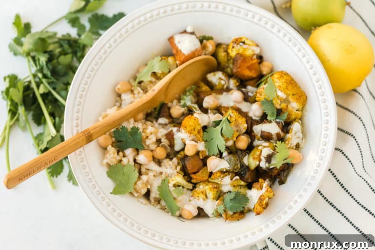 A beautifully presented anti-inflammatory veggie bowl with a wooden spoon for serving, showcasing the roasted vegetables, rice, and chickpeas with tahini sauce.
