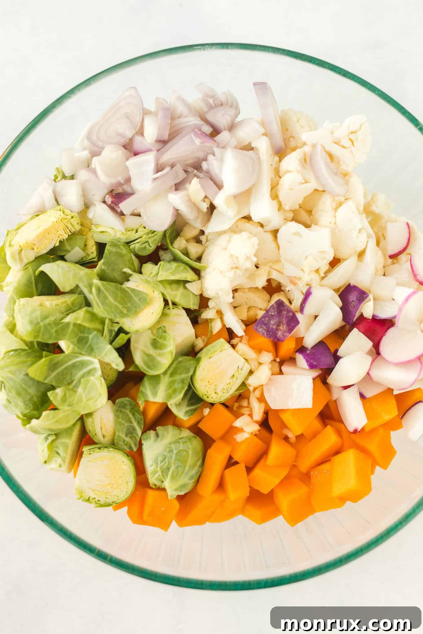 Various chopped anti-inflammatory vegetables including butternut squash, cauliflower, onion, and Brussels sprouts in a large mixing bowl, ready for seasoning.