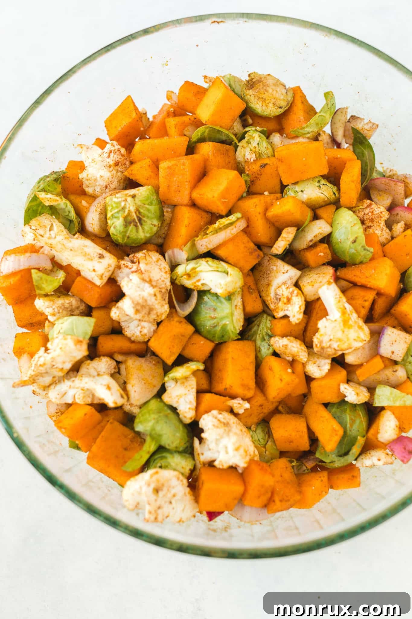 Chopped vegetables generously tossed with cooking oil and a vibrant anti-inflammatory spice blend in a large mixing bowl, preparing for roasting.