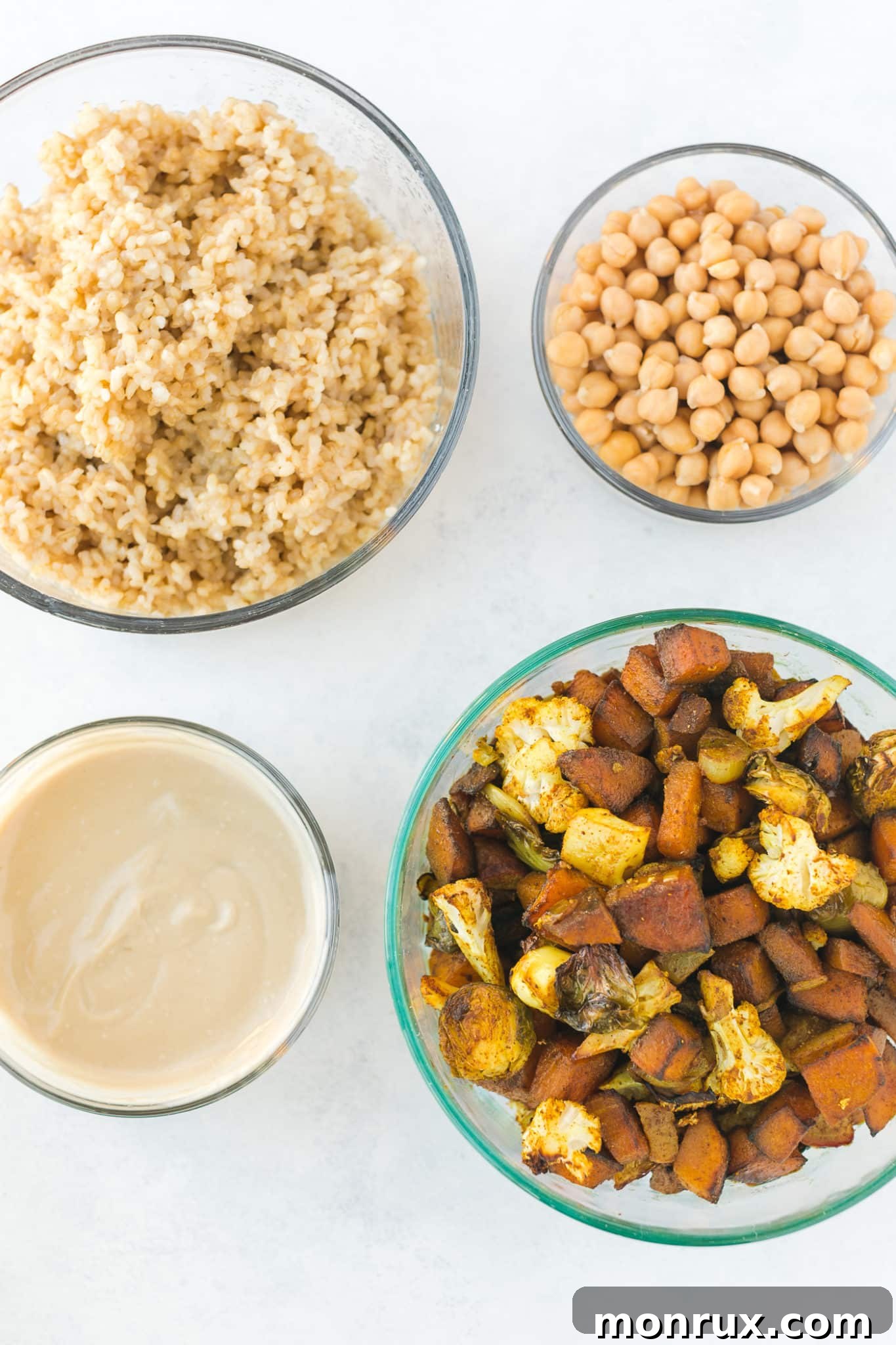 Individual glass meal prep containers filled with cooked brown rice, roasted vegetables, and chickpeas, ready for storage and future assembly.