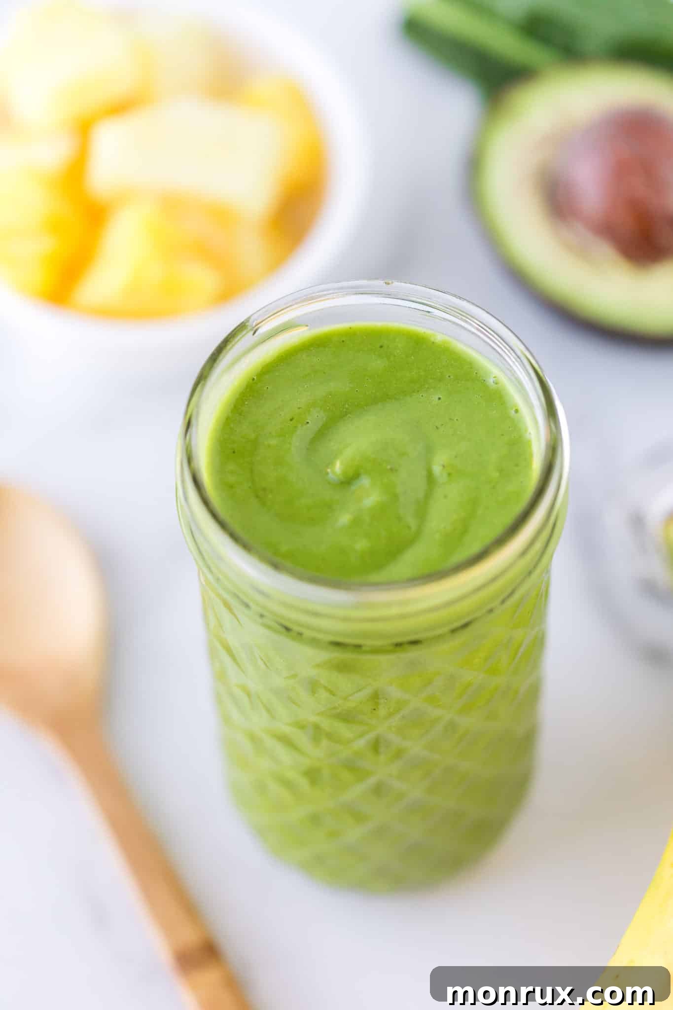 Green smoothie served in a clear glass, garnished with a slice of pineapple and fresh mint.