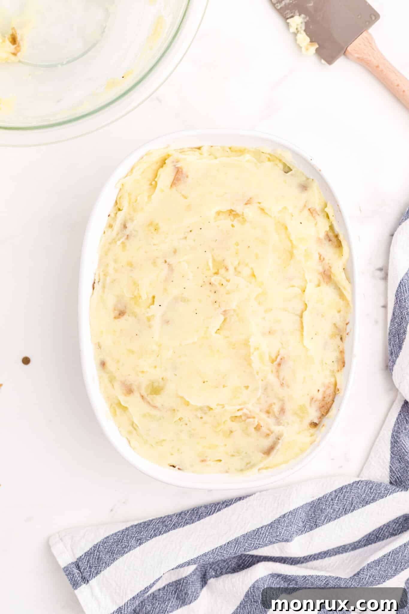 A baking dish filled with the lentil and vegetable base, topped with a smooth layer of mashed potatoes, ready for the oven.