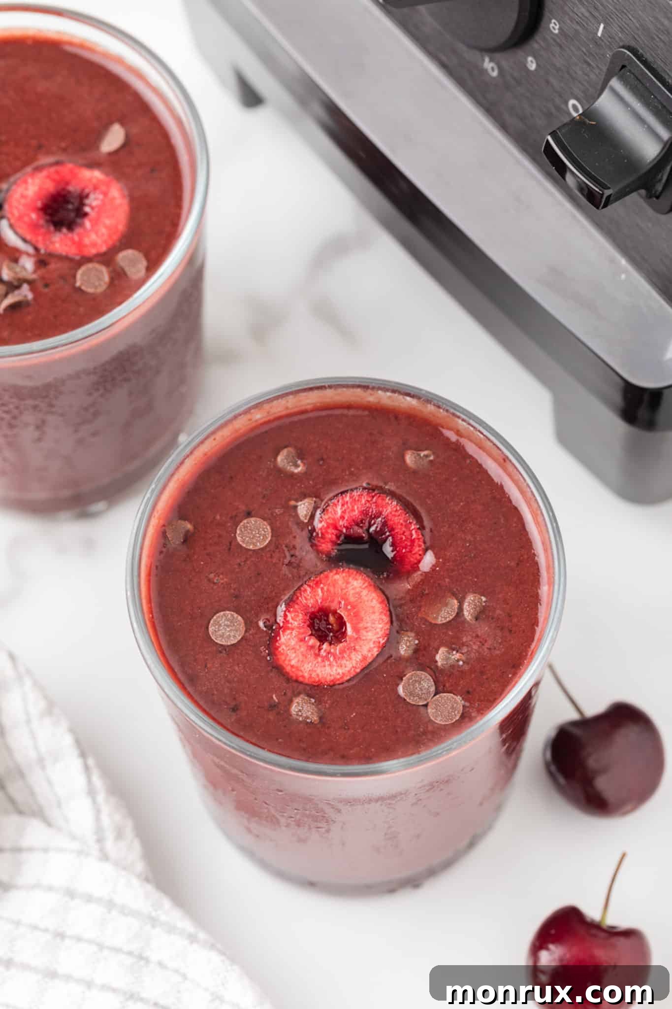 Two glasses of rich chocolate cherry smoothie, garnished with fresh cherries.