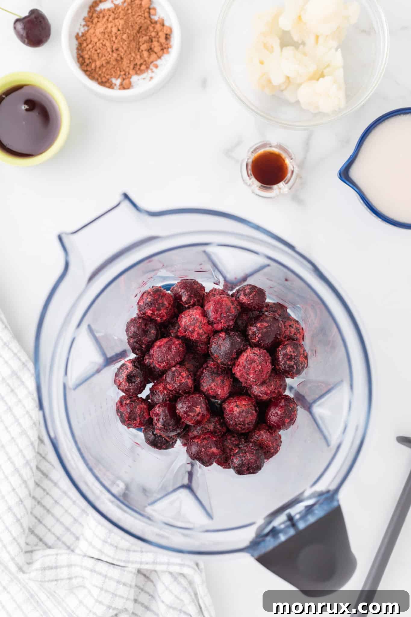 Frozen cherries and liquid being added to a high-speed blender for a chocolate cherry smoothie.