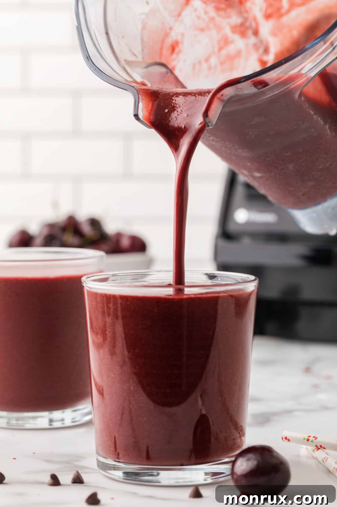 Pouring a finished chocolate cherry smoothie into a tall glass.