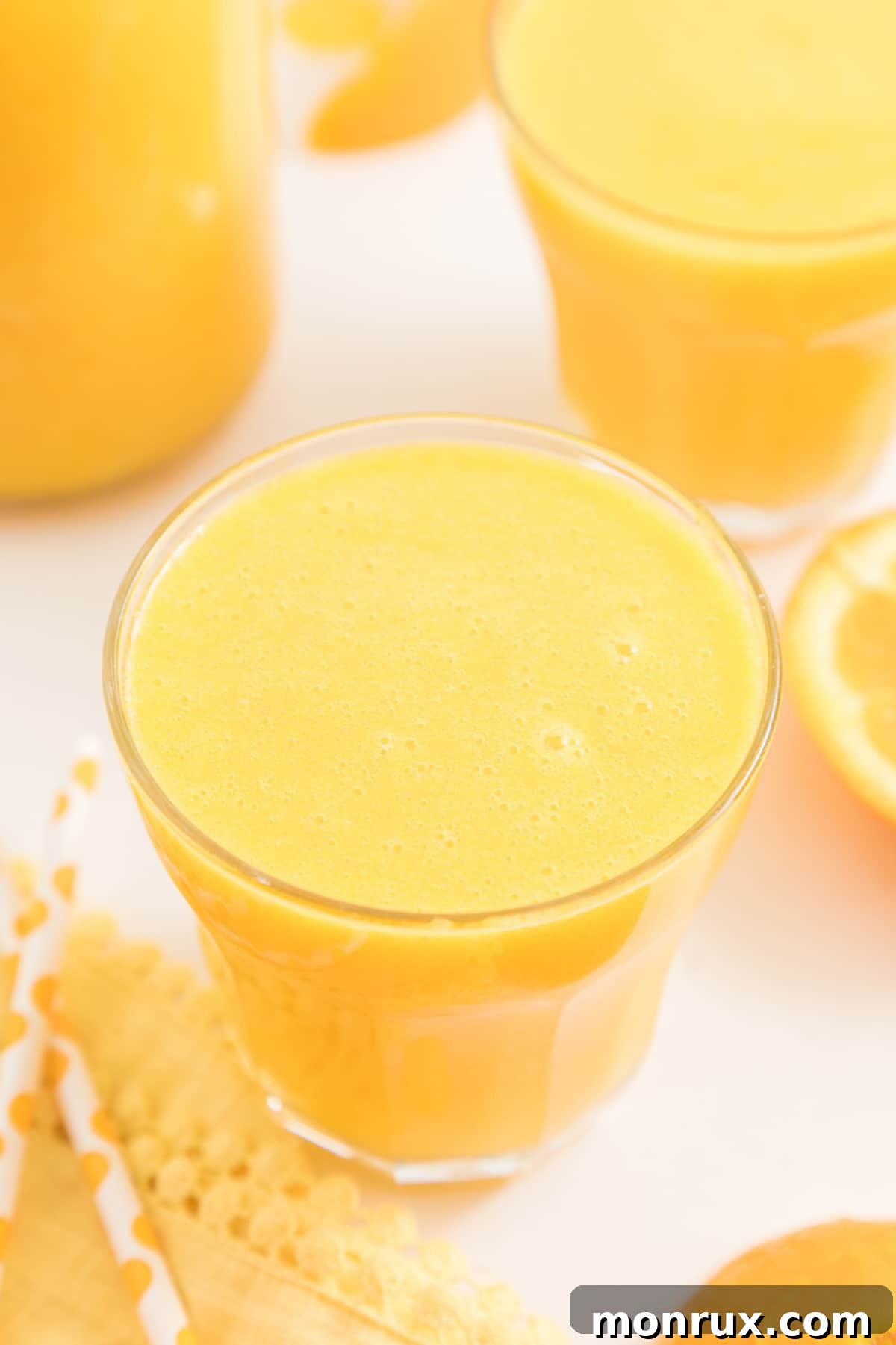 blended orange juice served in low glass on table with fresh oranges.
