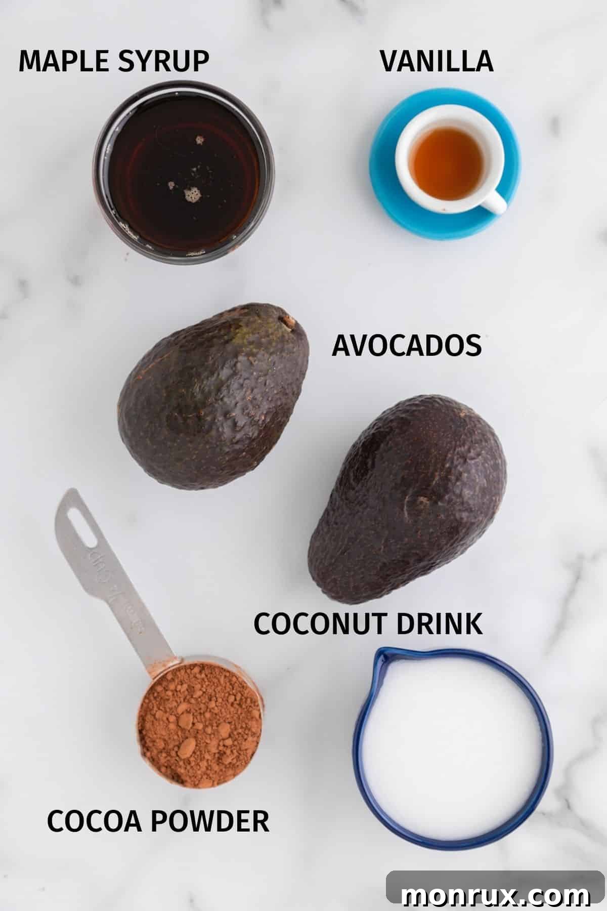 Ingredients for avocado vegan ice cream set on a white surface, including avocados, cocoa powder, maple syrup, and plant milk.