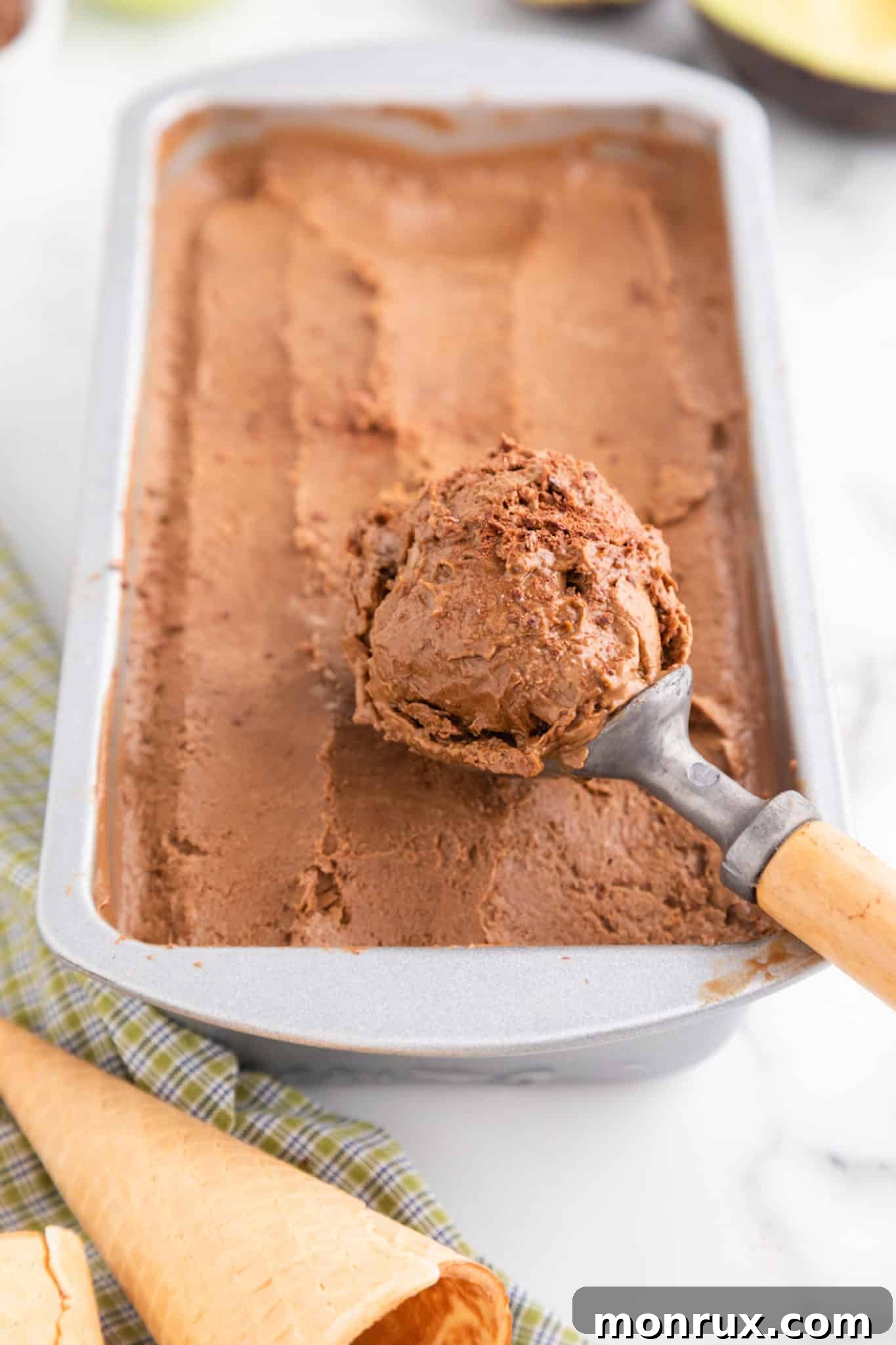 An ice cream scoop filled with chocolate avocado ice cream from a metal loaf pan, ready to be served.
