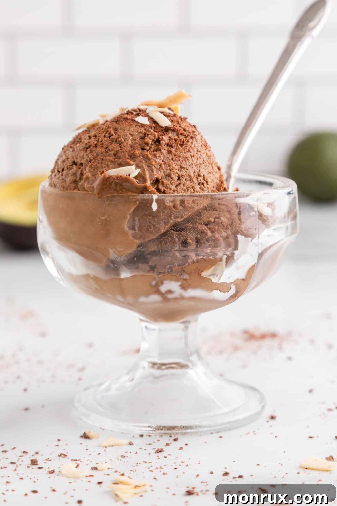 Side view of a glass parfait dish holding a spoon and two scoops of chocolate avocado ice cream, showing its rich texture.