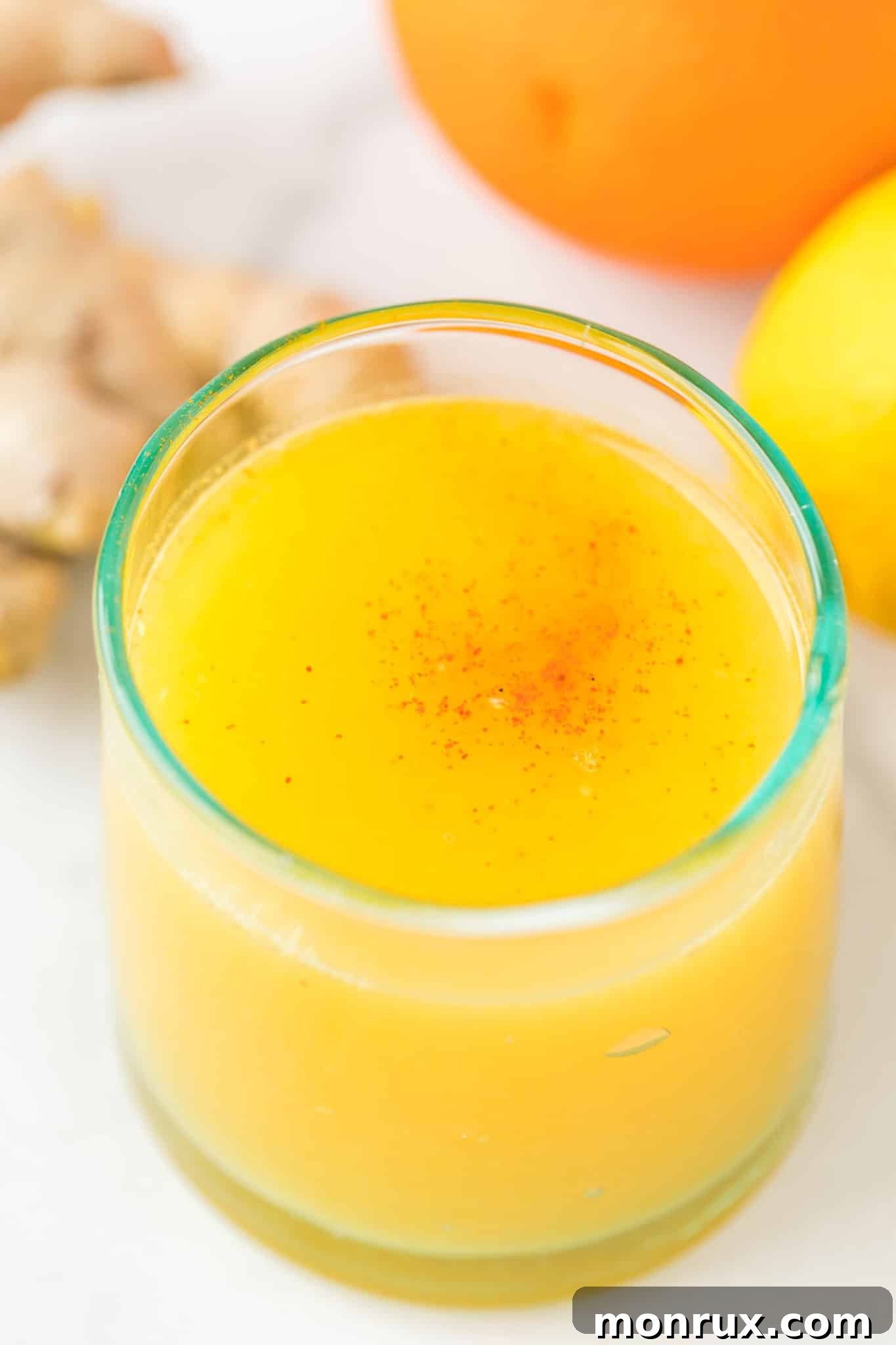 A beautifully presented orange ginger lemon juice shot in a clear glass, subtly sprinkled with cayenne pepper on top, against a warm, inviting background.