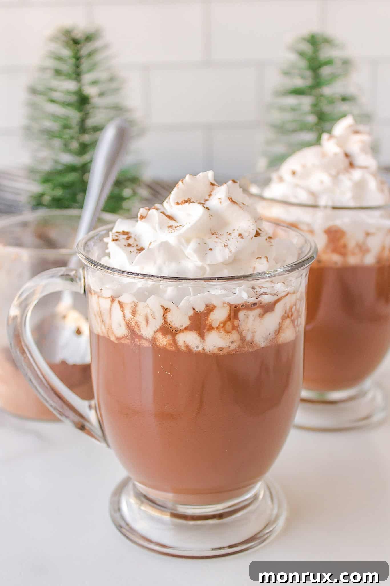 A beautifully styled cup of healthy oat milk hot cocoa topped with fluffy coconut whipped cream, inviting you to take a sip.