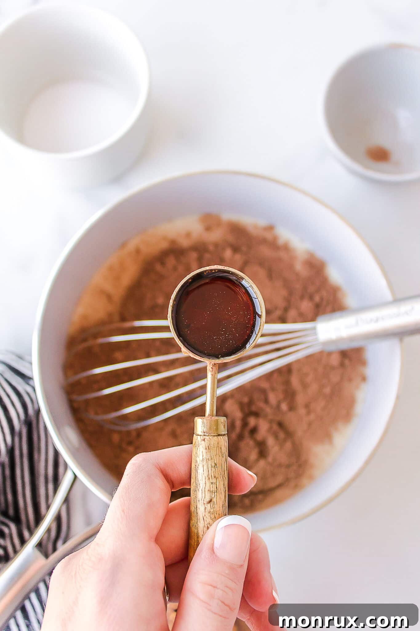 A hand adding a stream of golden maple syrup into the warming dairy-free milk in a saucepan, beginning to mix the hot chocolate ingredients.