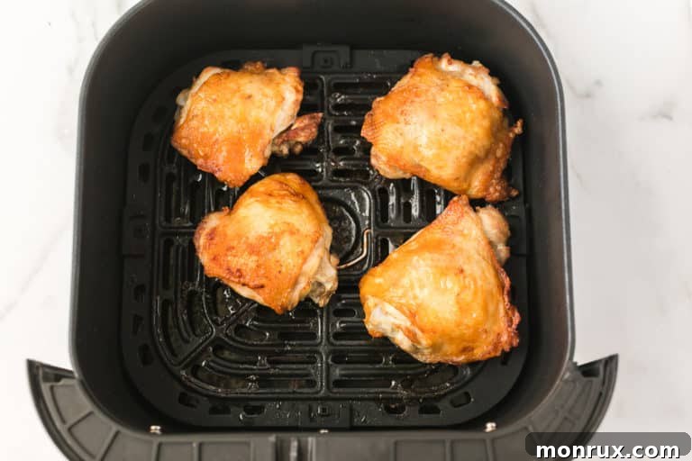 four cooked chicken thighs in the basket of an air fryer