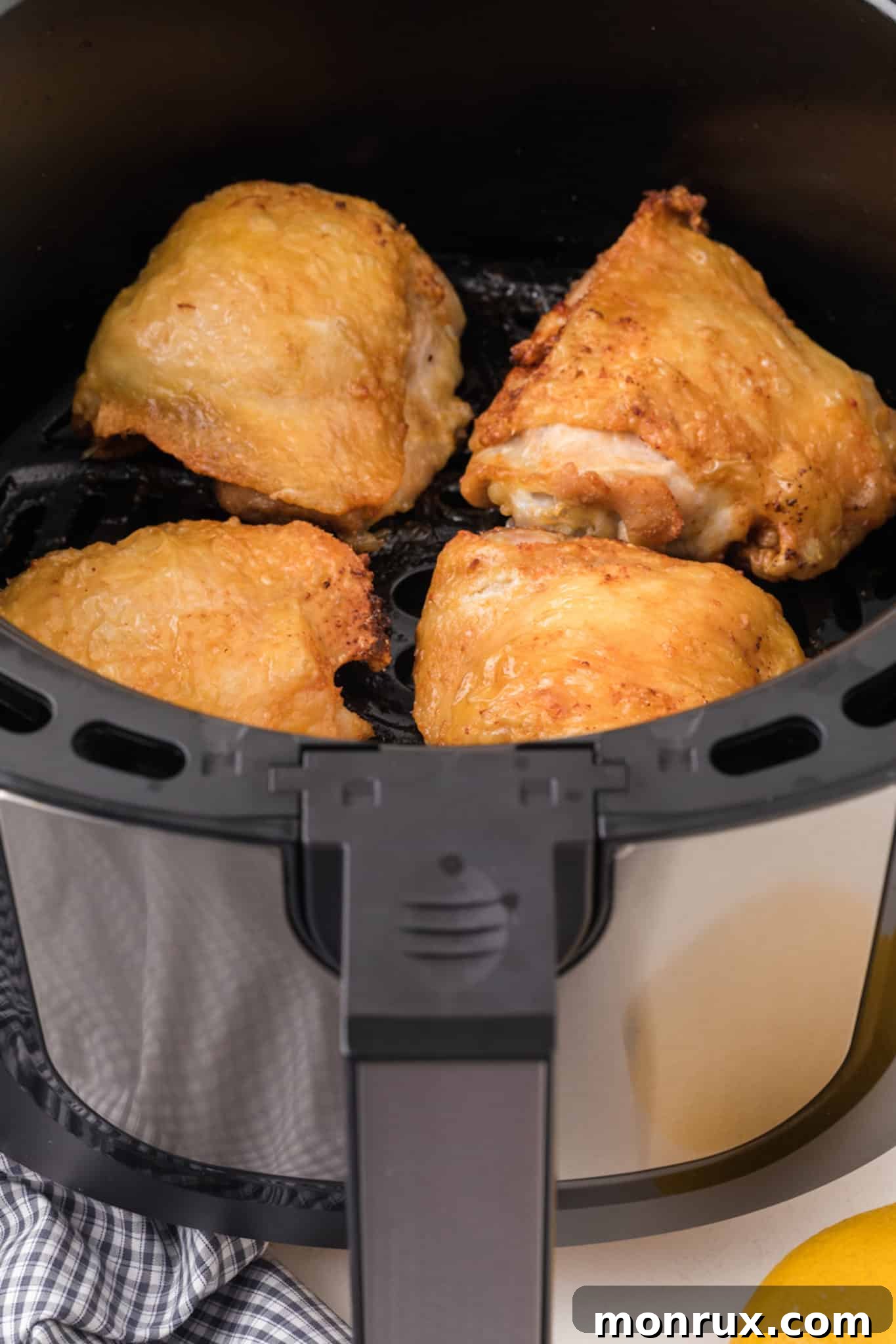 Three perfectly cooked, crispy chicken thighs resting in an air fryer basket after cooking.