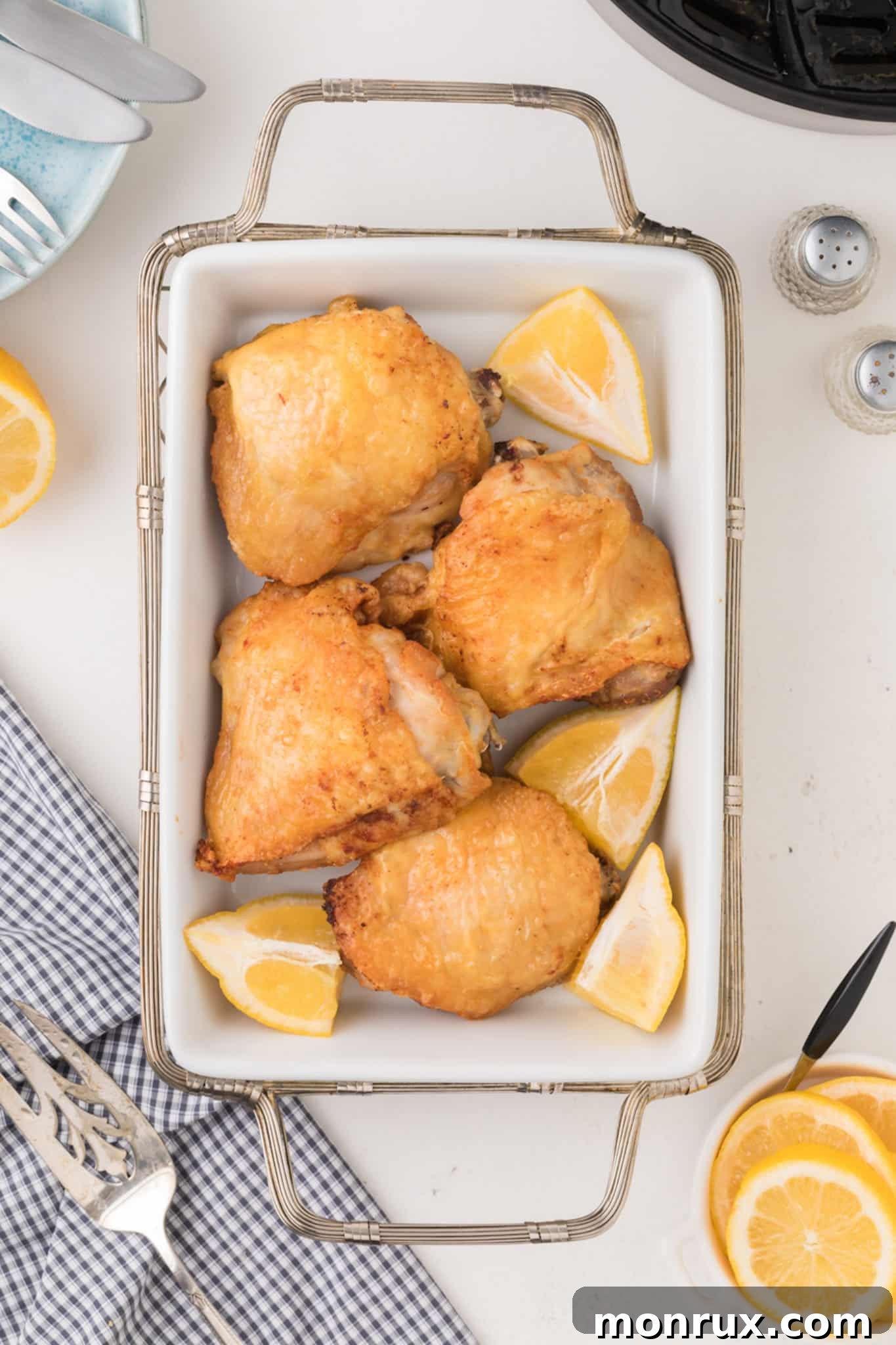 A platter of air-fried bone-in chicken thighs, garnished with fresh lemon wedges and herbs, ready for serving.