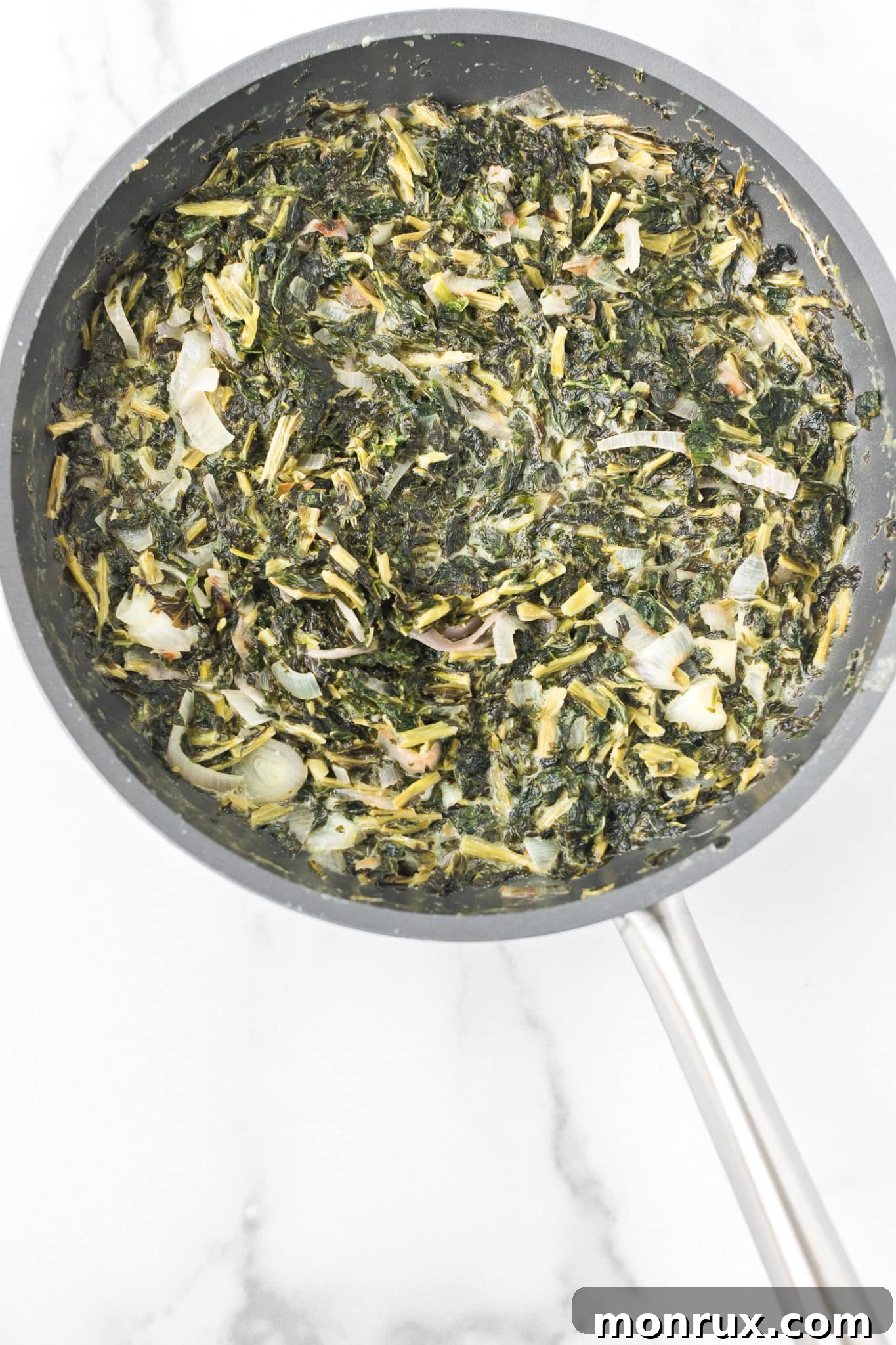 A vibrant skillet filled with creamy vegan kale, garnished with fresh herbs, ready to be served.