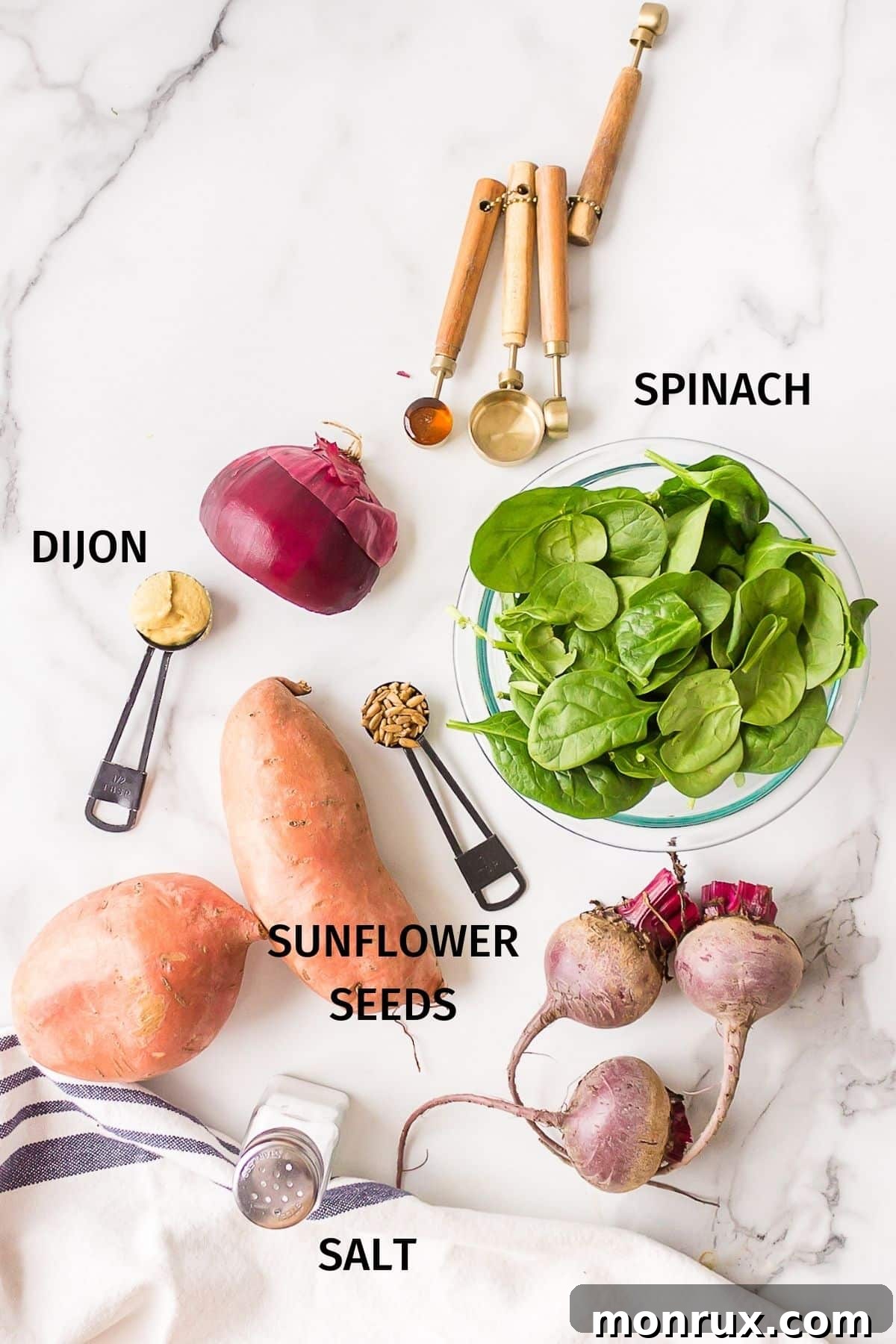 Assortment of fresh ingredients for sweet potato spinach salad, including sweet potatoes, beets, spinach, red onion, and dressing components, laid out on a clean white surface.