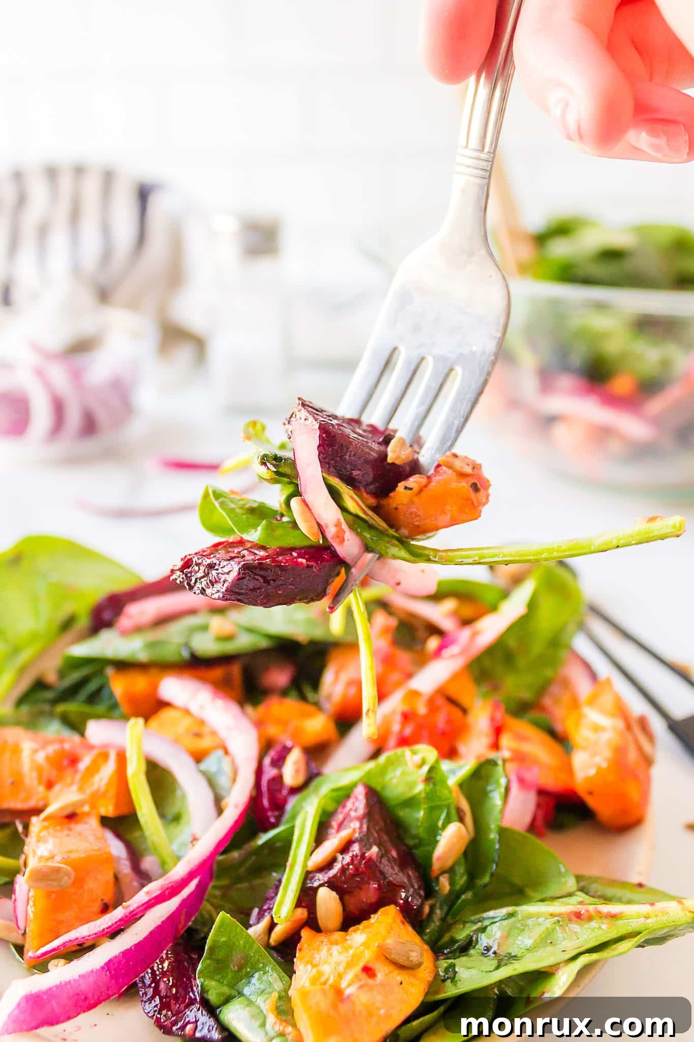 A fork lifts a bite of sweet potato and beet salad with spinach, highlighting the vibrant colors and textures.