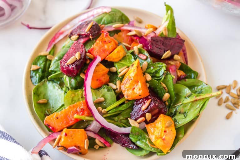 Close up of diced beets and sweet potatoes on a dressed spinach salad, showcasing the vibrant colors and appealing textures of the dish.