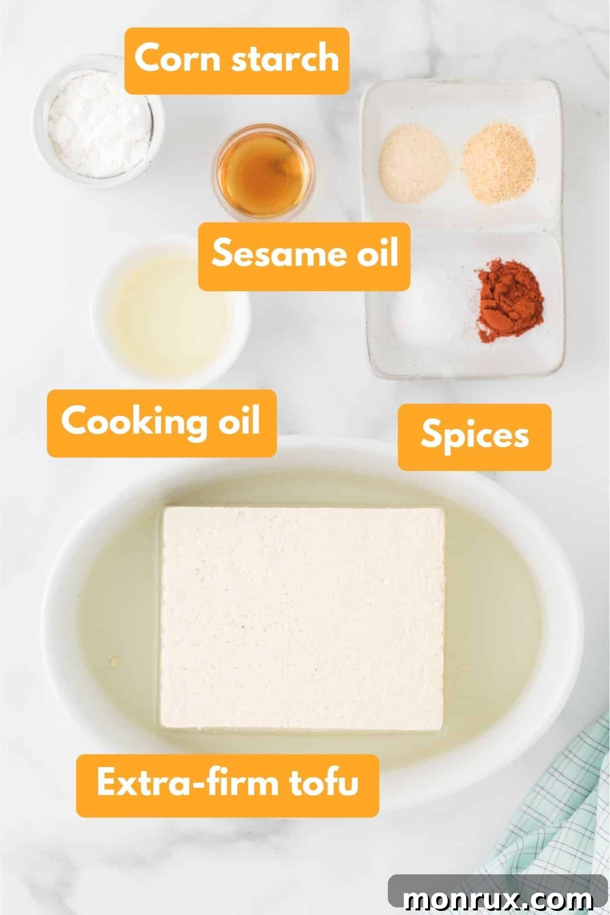 A selection of ingredients laid out, including a block of extra-firm tofu, a bottle of oil, and small bowls of spices and cornstarch.
