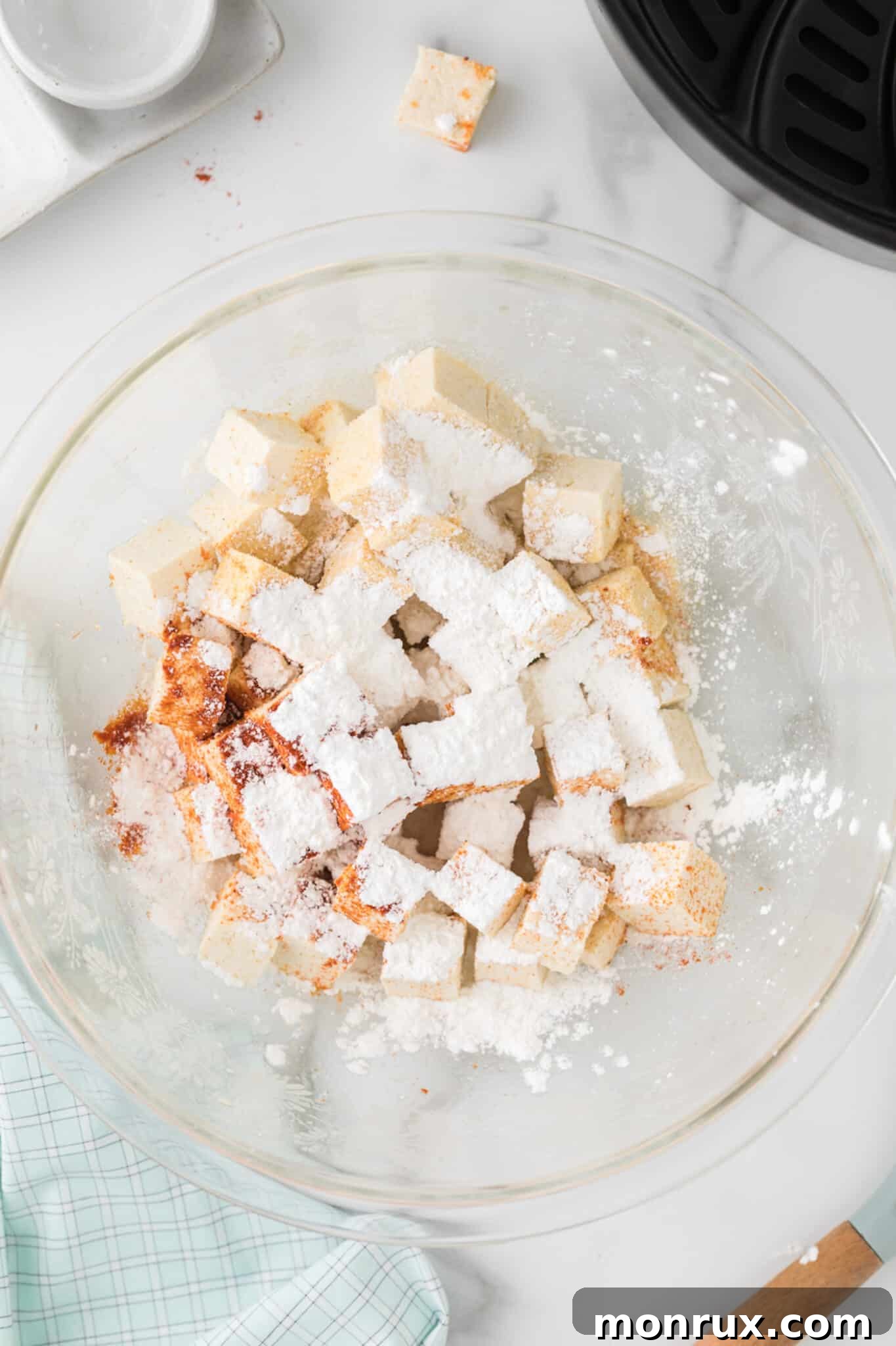 Tofu cubes in a mixing bowl with a dusting of cornstarch and a blend of spices.