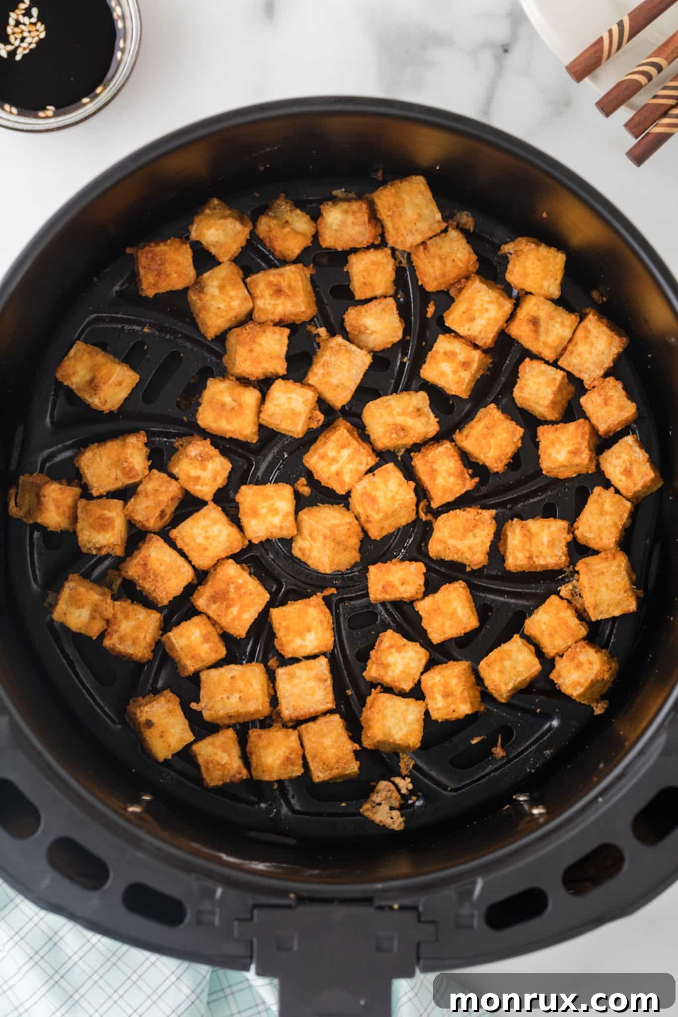 Close-up of golden, crispy air-fried tofu in an air fryer basket, showcasing its texture.
