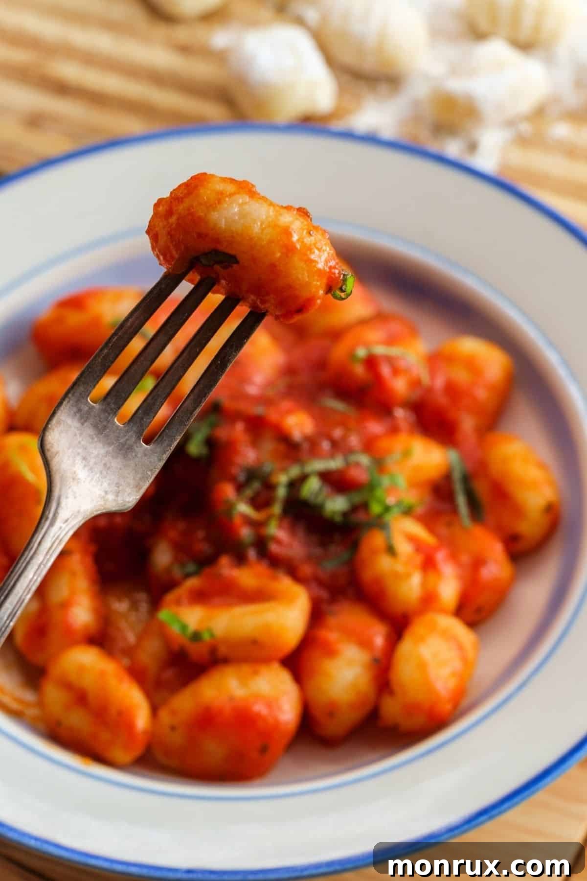 A fork lifts a piece of cooked vegan gnocchi covered in vibrant red marinara sauce, showcasing its tender texture and delicious coating.