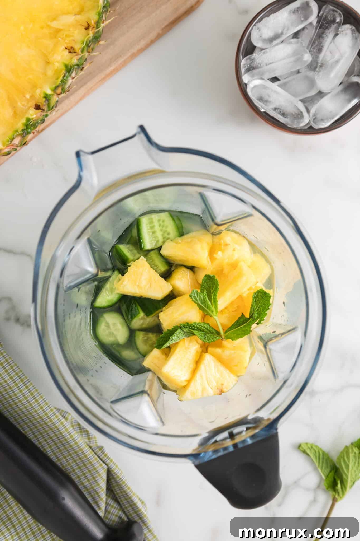 A blender jar filled with a colorful mix of cucumber, pineapple, coconut water, mint, and lime, ready to be blended.