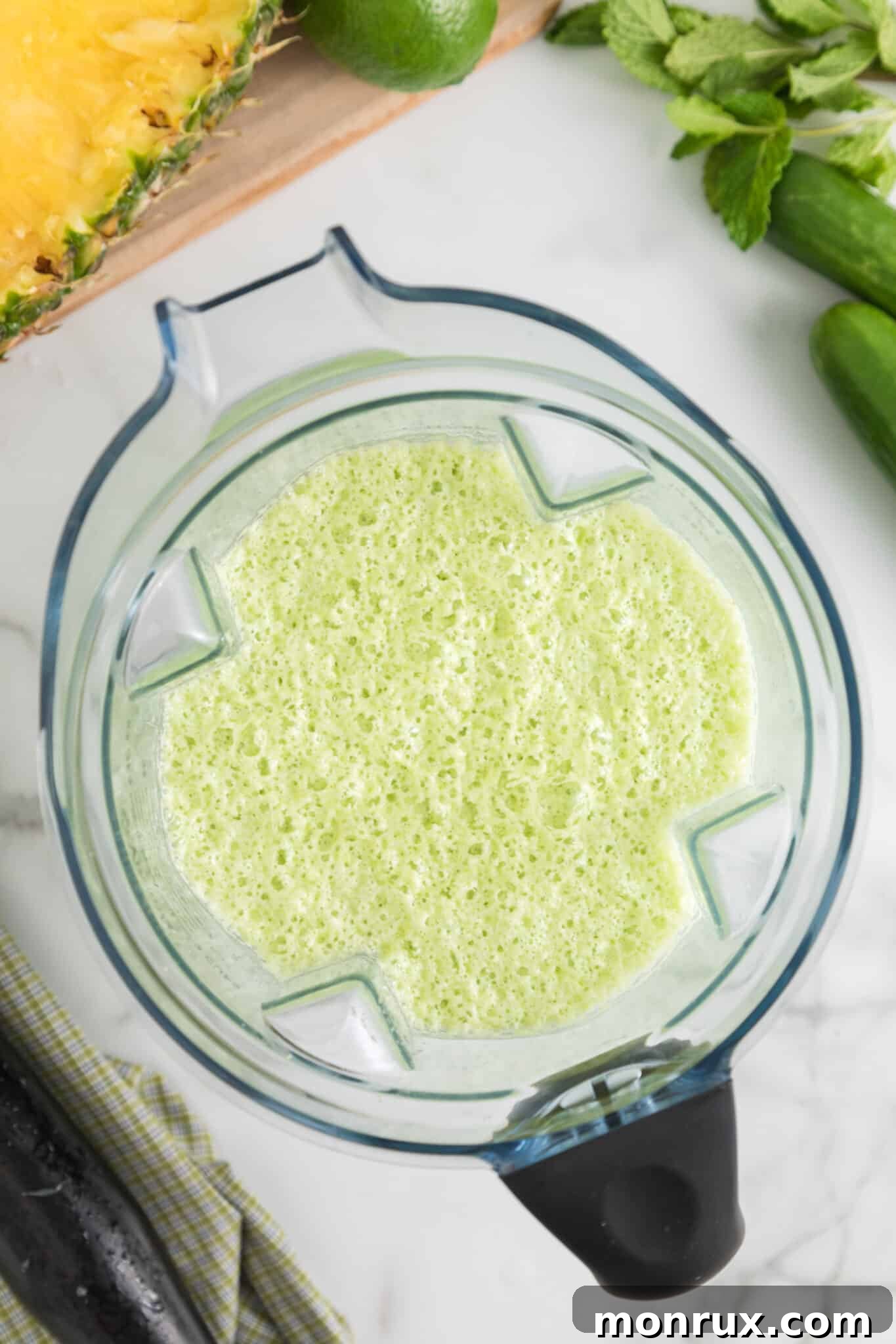 A high-speed blender container filled with a perfectly blended, smooth, and green cucumber pineapple smoothie.