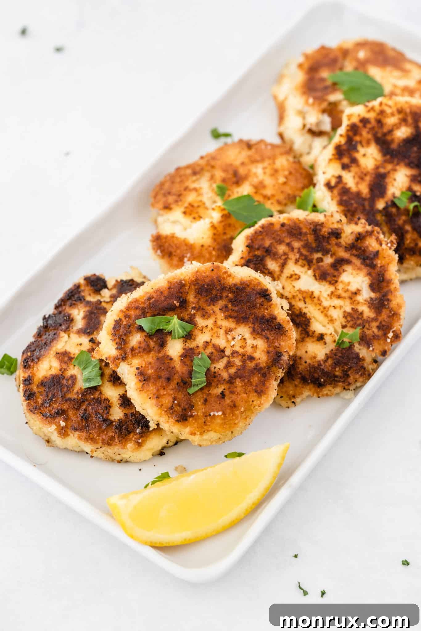 Homemade gluten-free Whole30 crab cakes cooked and served on a white platter, garnished with fresh herbs and lemon wedges.