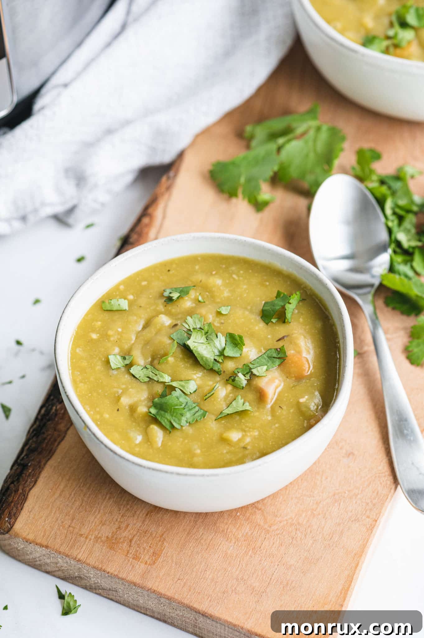 A comforting bowl of Instant Pot Split Pea and Ham Soup, garnished with fresh herbs, resting on a rustic kitchen counter with a spoon.