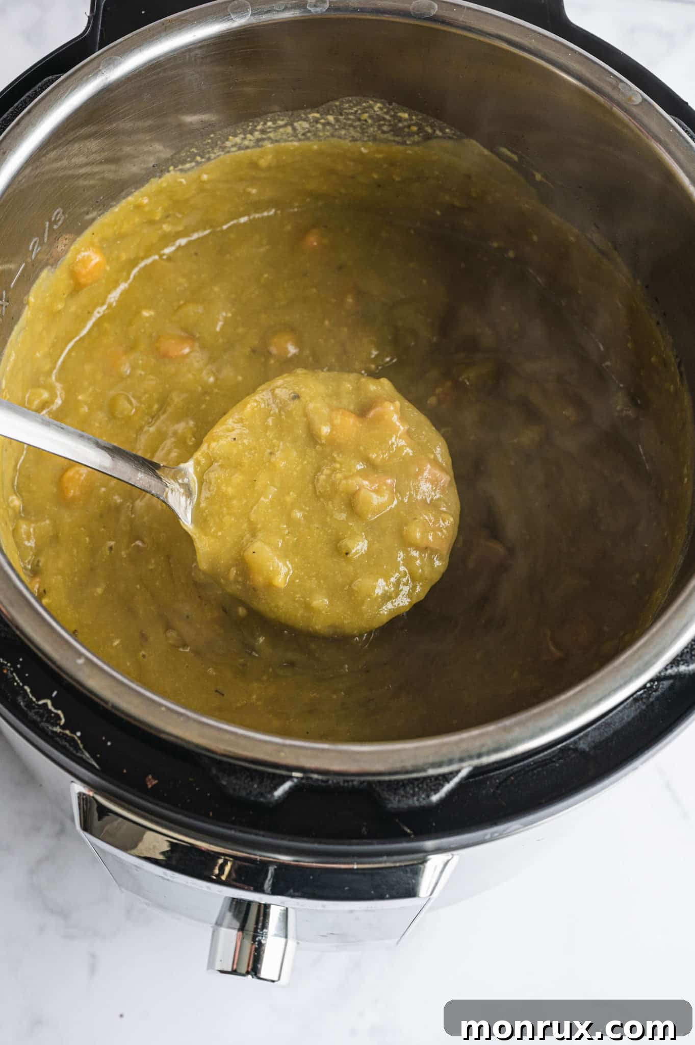 A serving spoon lifting a rich, thick portion of Instant Pot cooked split pea soup from a bowl, highlighting its hearty texture.