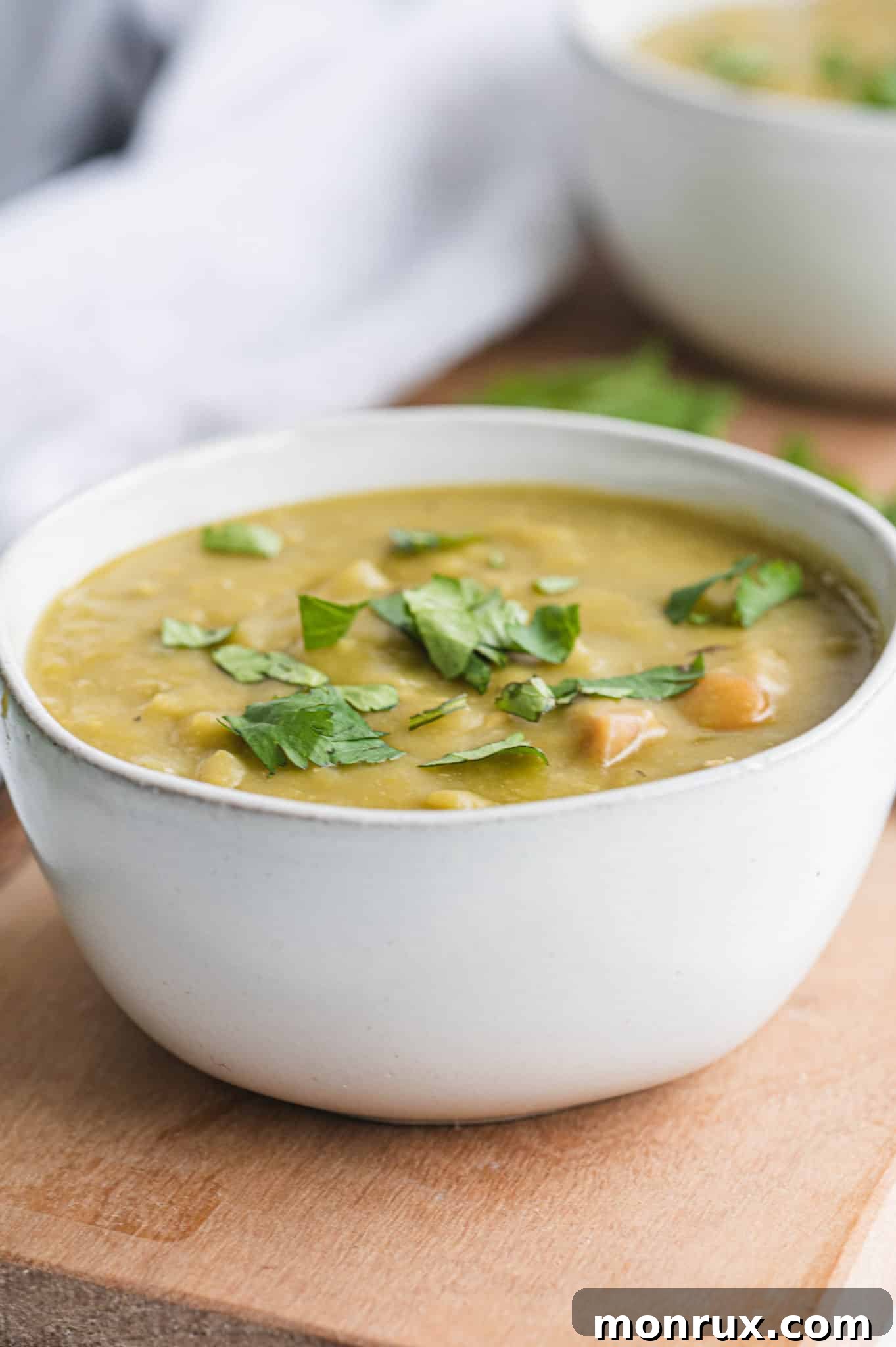 A white ceramic bowl filled with creamy Instant Pot Split Pea and Ham Soup, garnished with fresh chopped parsley, ready to be enjoyed.