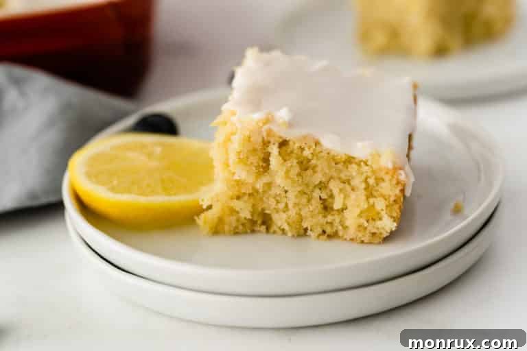 A slice of delectable lemon cake on a white plate with fresh lemon garnish.