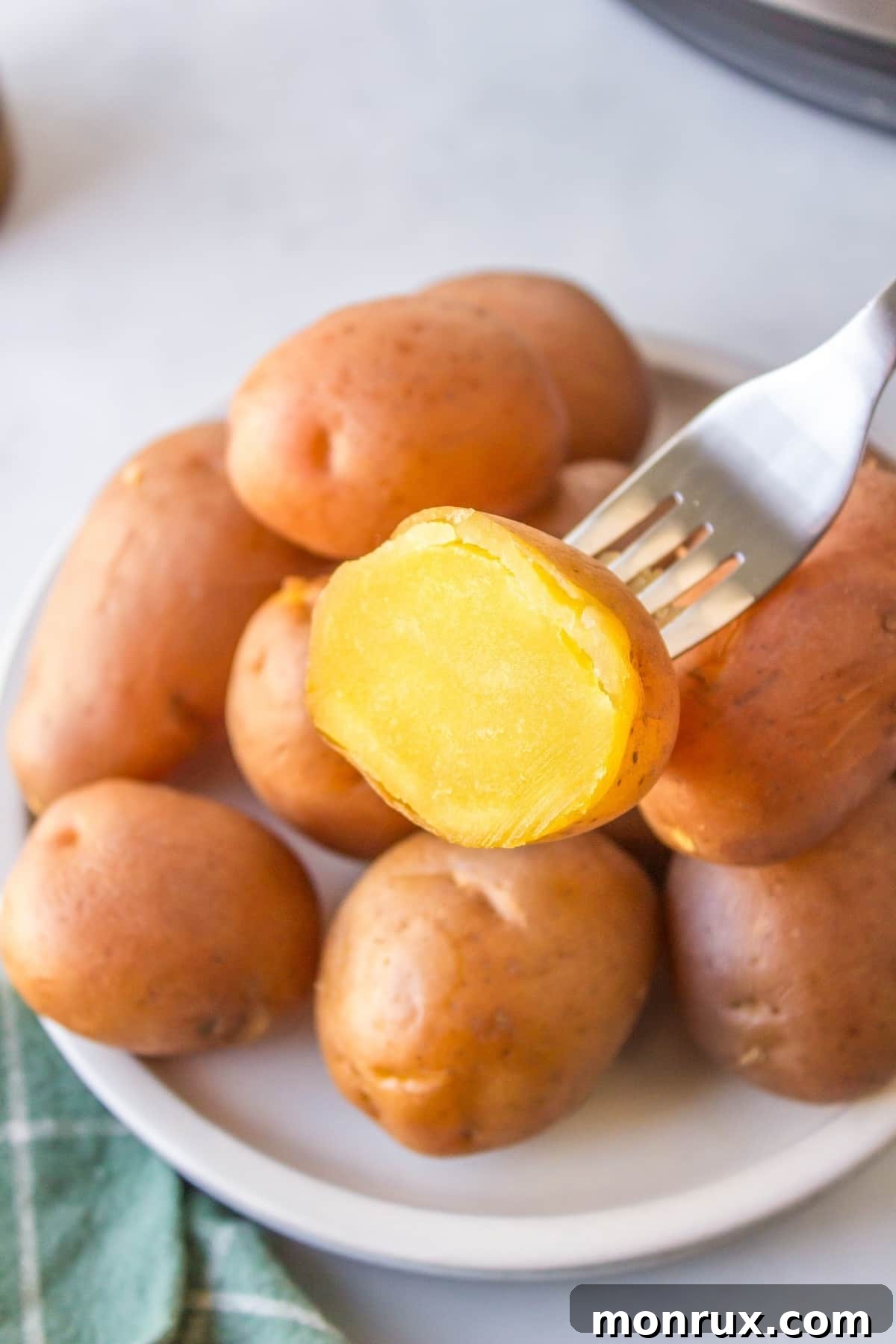 instant pot gold potato cut in half on a fork with other cooked potatoes.
