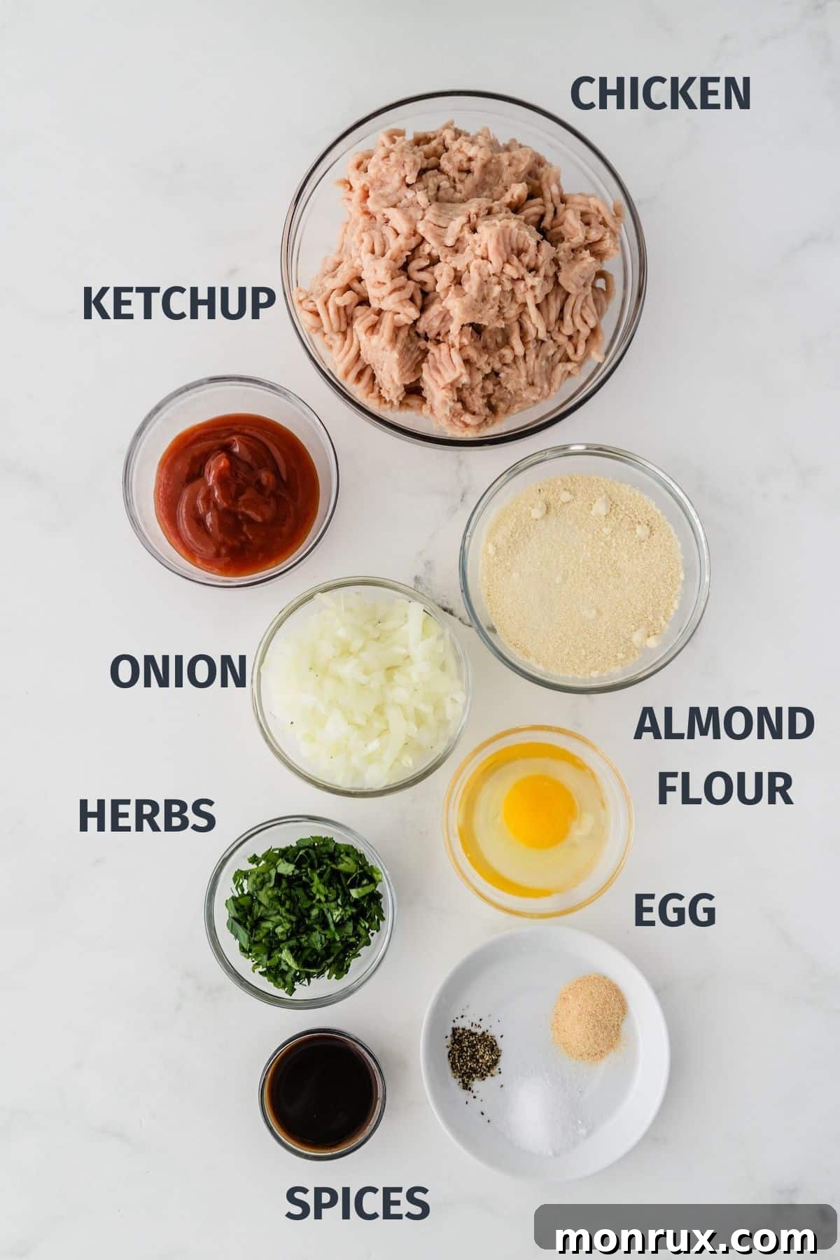 A collection of fresh ingredients laid out on a kitchen counter for making healthy chicken meatloaf, including ground chicken, almond flour, onion, and spices.